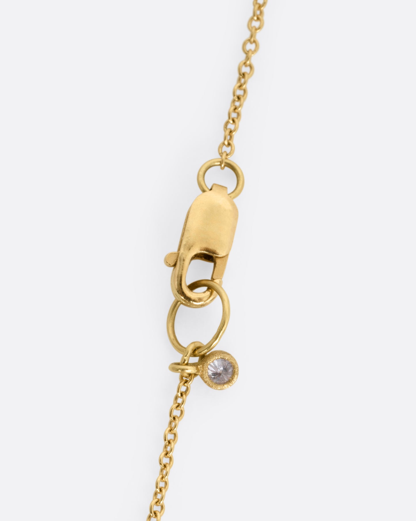 The clasp on a yellow gold necklace with a diamond charm, shown close up.