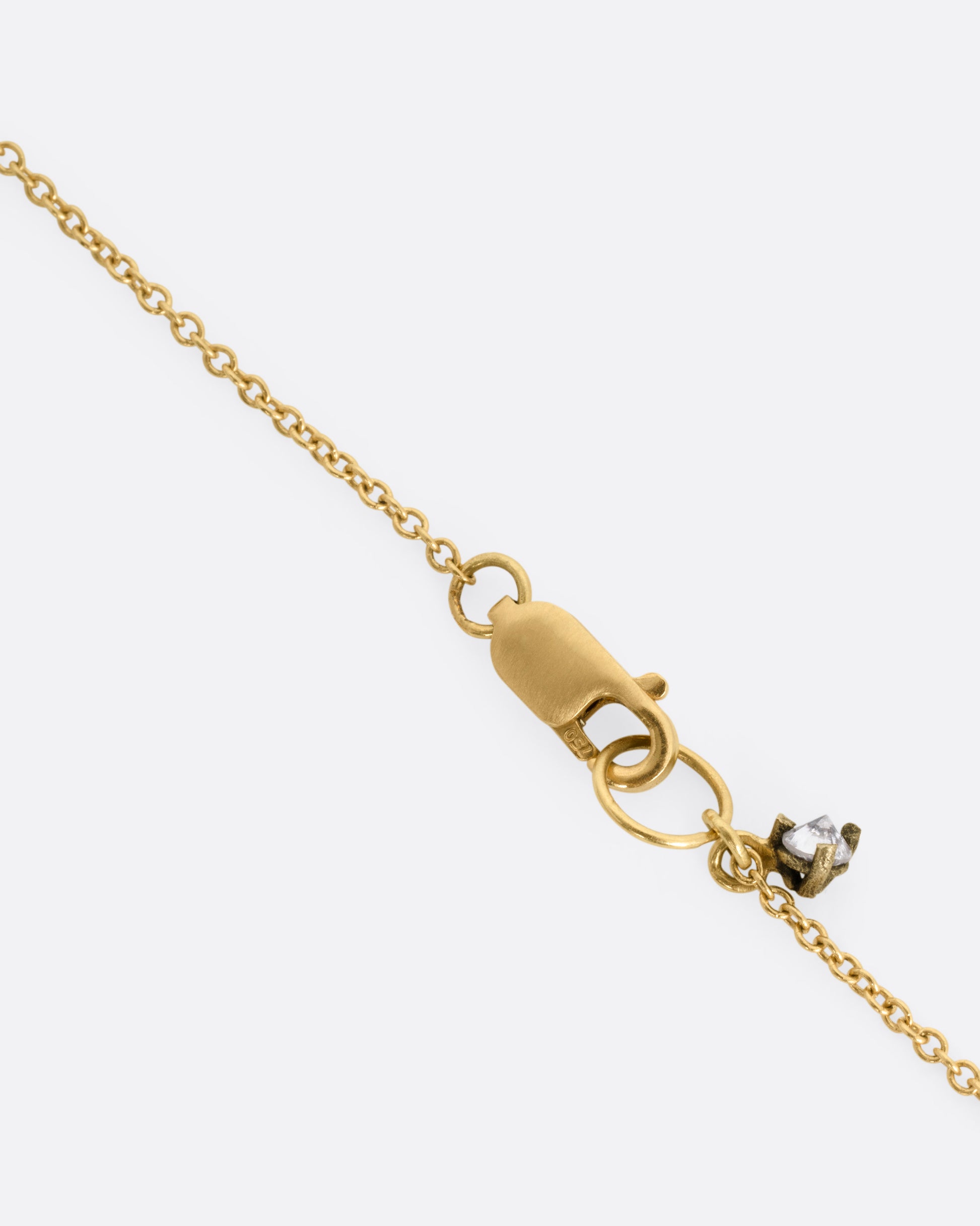 A close up of a clasp on a yellow gold cable chain necklace with a diamond dangle.