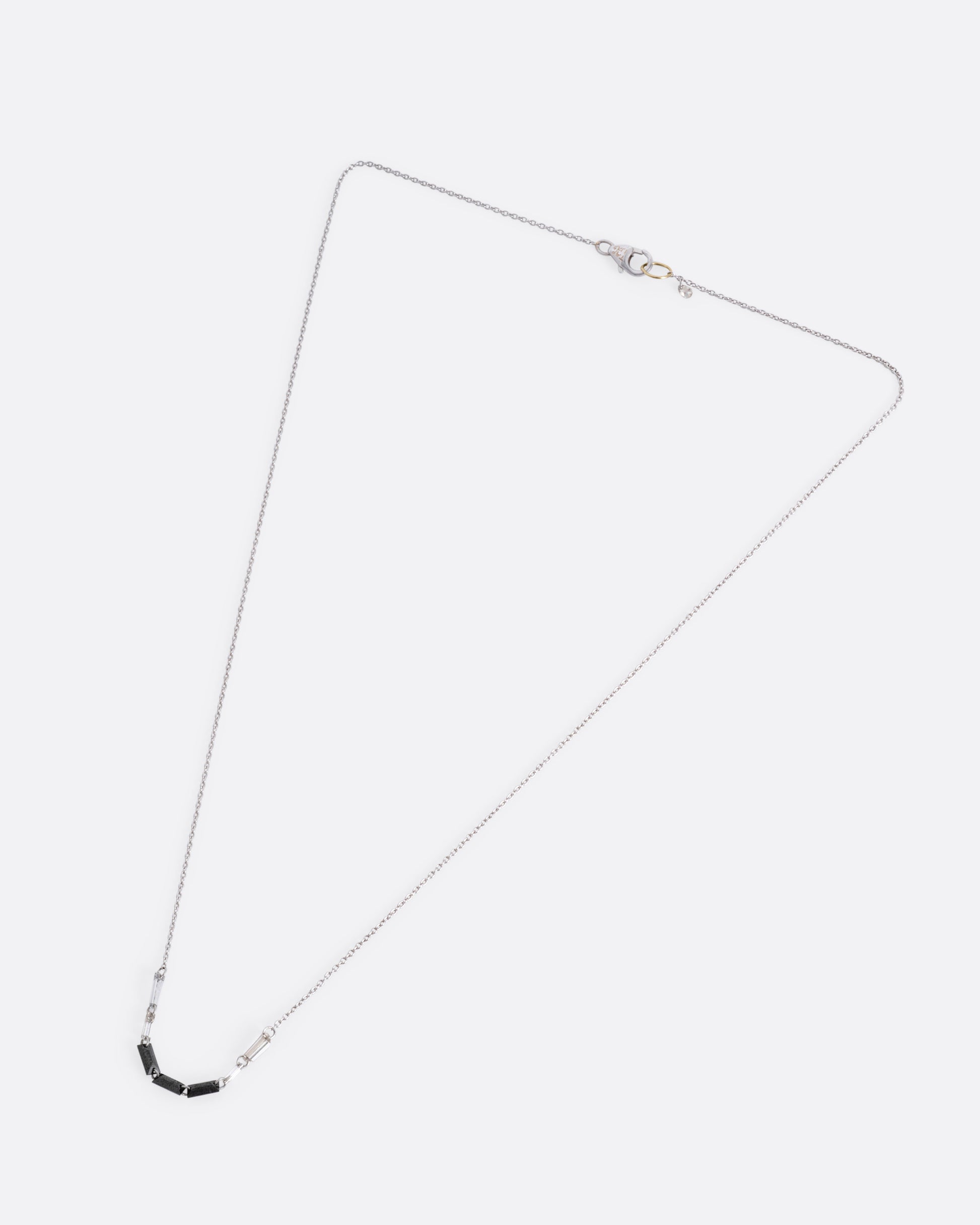 A white gold cable chain with black and white baguette diamonds connected by platinum jump rings, shown from the front.