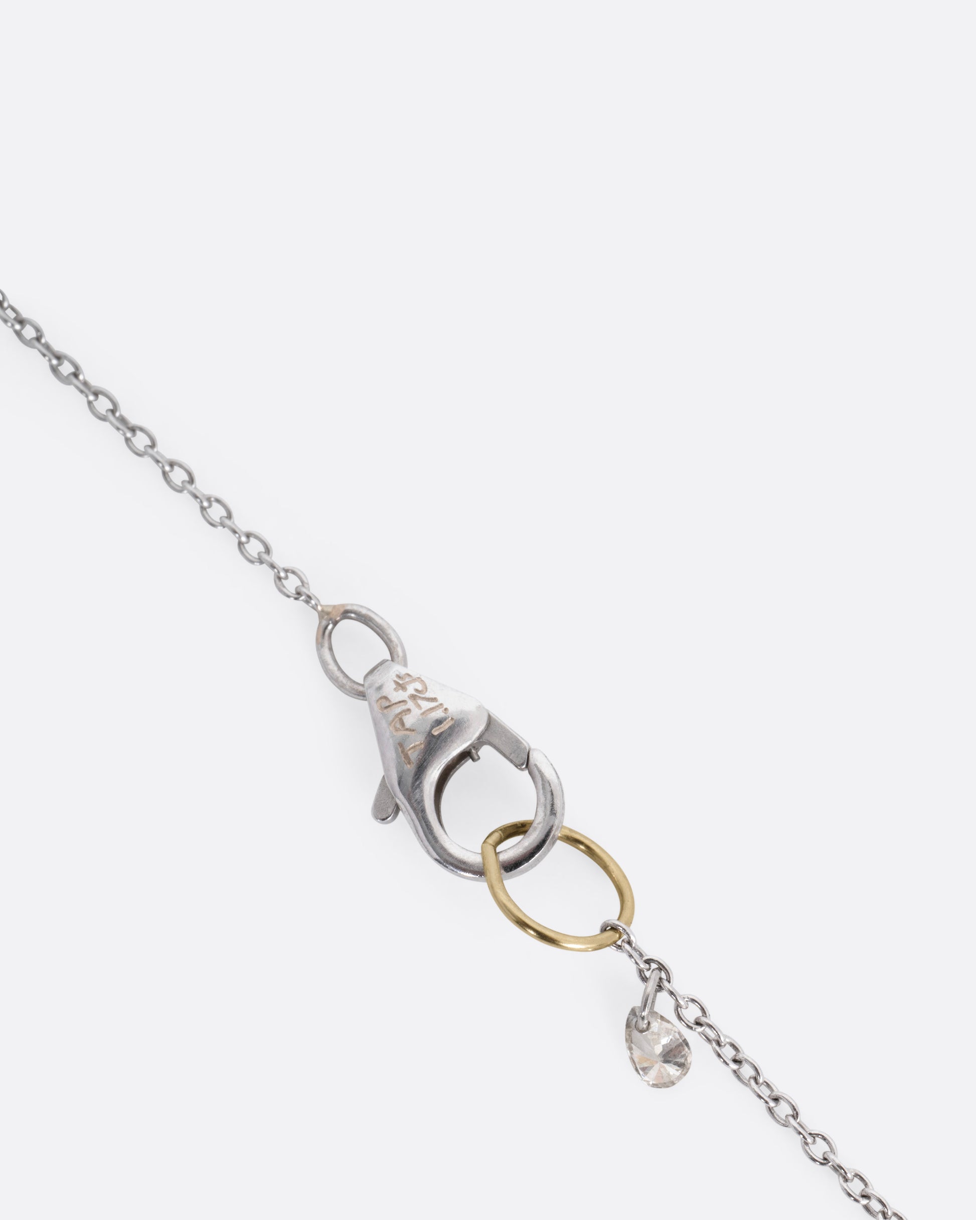 A close up of a white gold clasp with a diamond dangle and yellow gold jump ring.