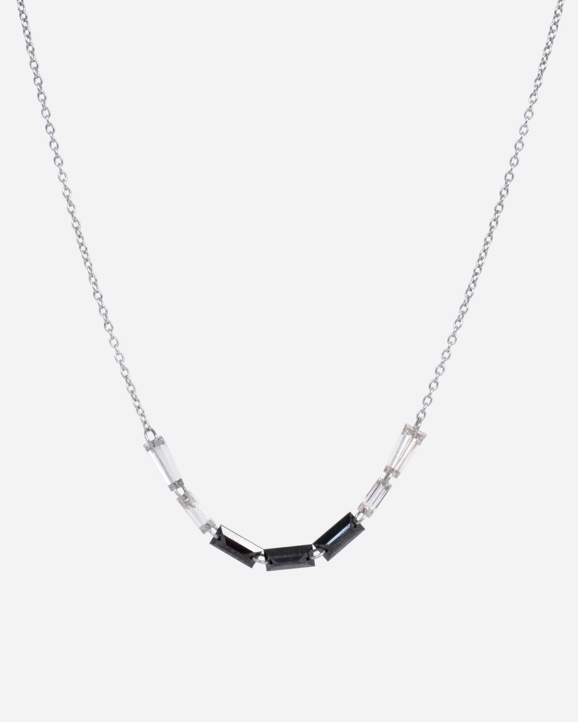 A white gold cable chain with black and white baguette diamonds connected by platinum jump rings, shown from the front.