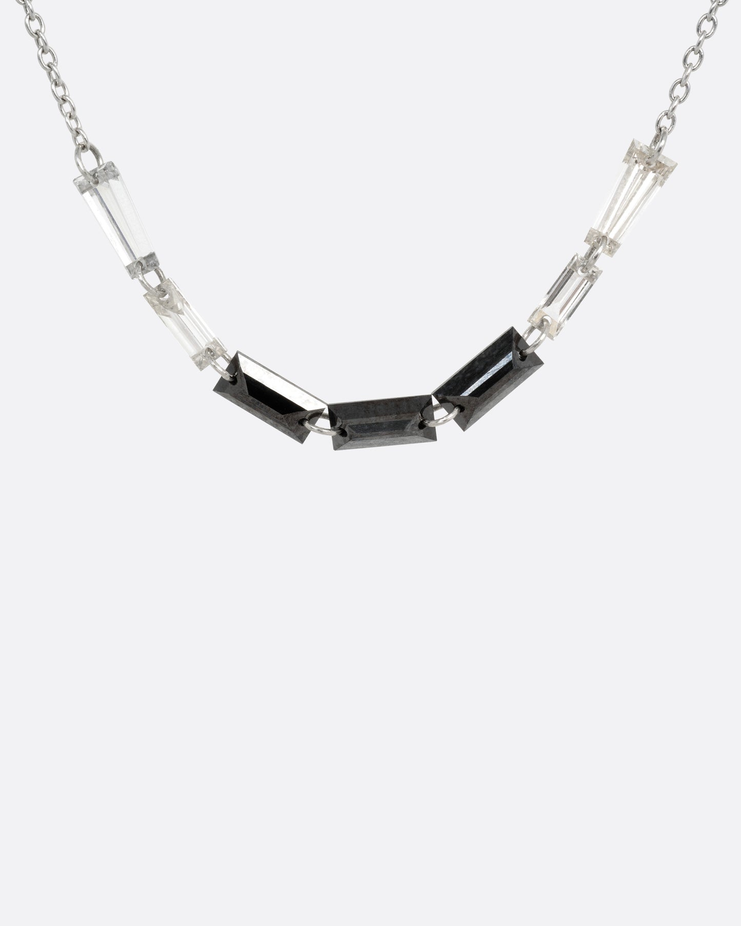 A white gold cable chain with black and white baguette diamonds connected by platinum jump rings, shown from the front.