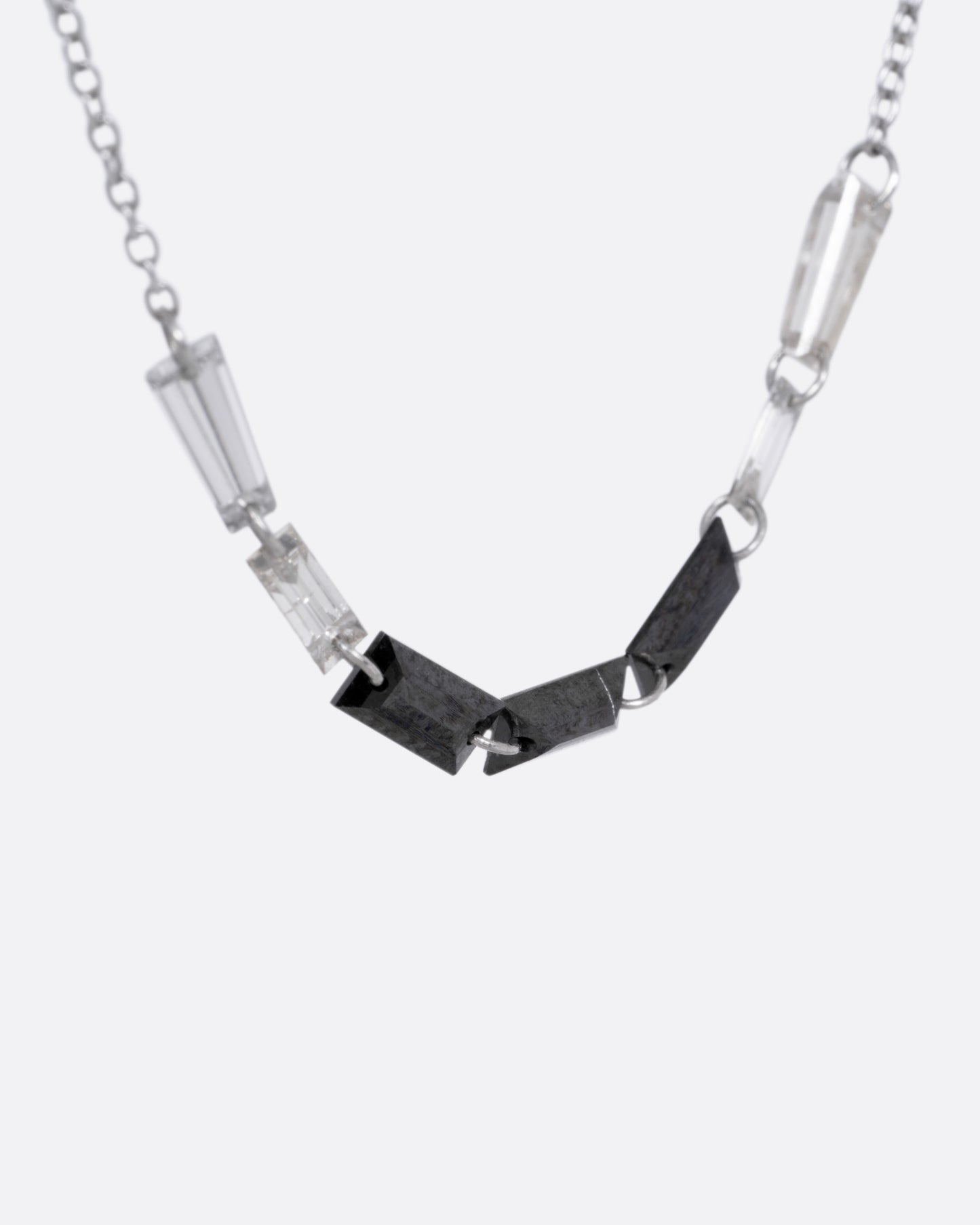A white gold cable chain with black and white baguette diamonds connected by platinum jump rings, shown from the side.