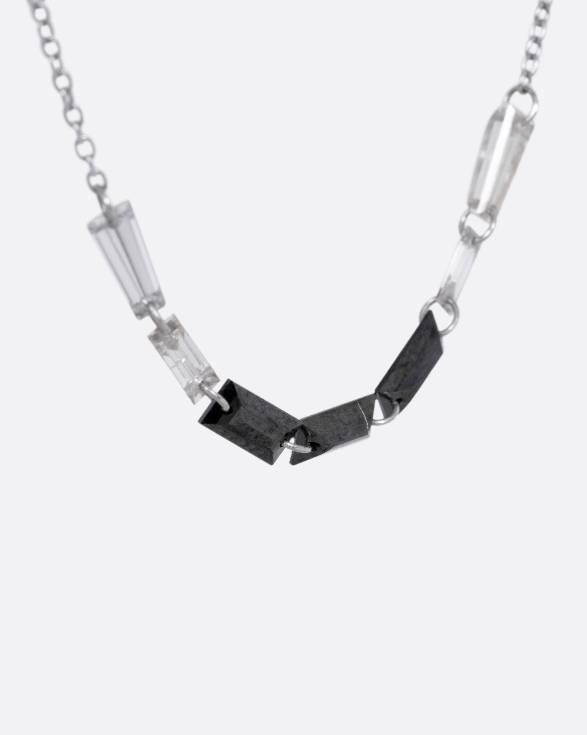 A white gold cable chain with black and white baguette diamonds connected by platinum jump rings, shown from the side.