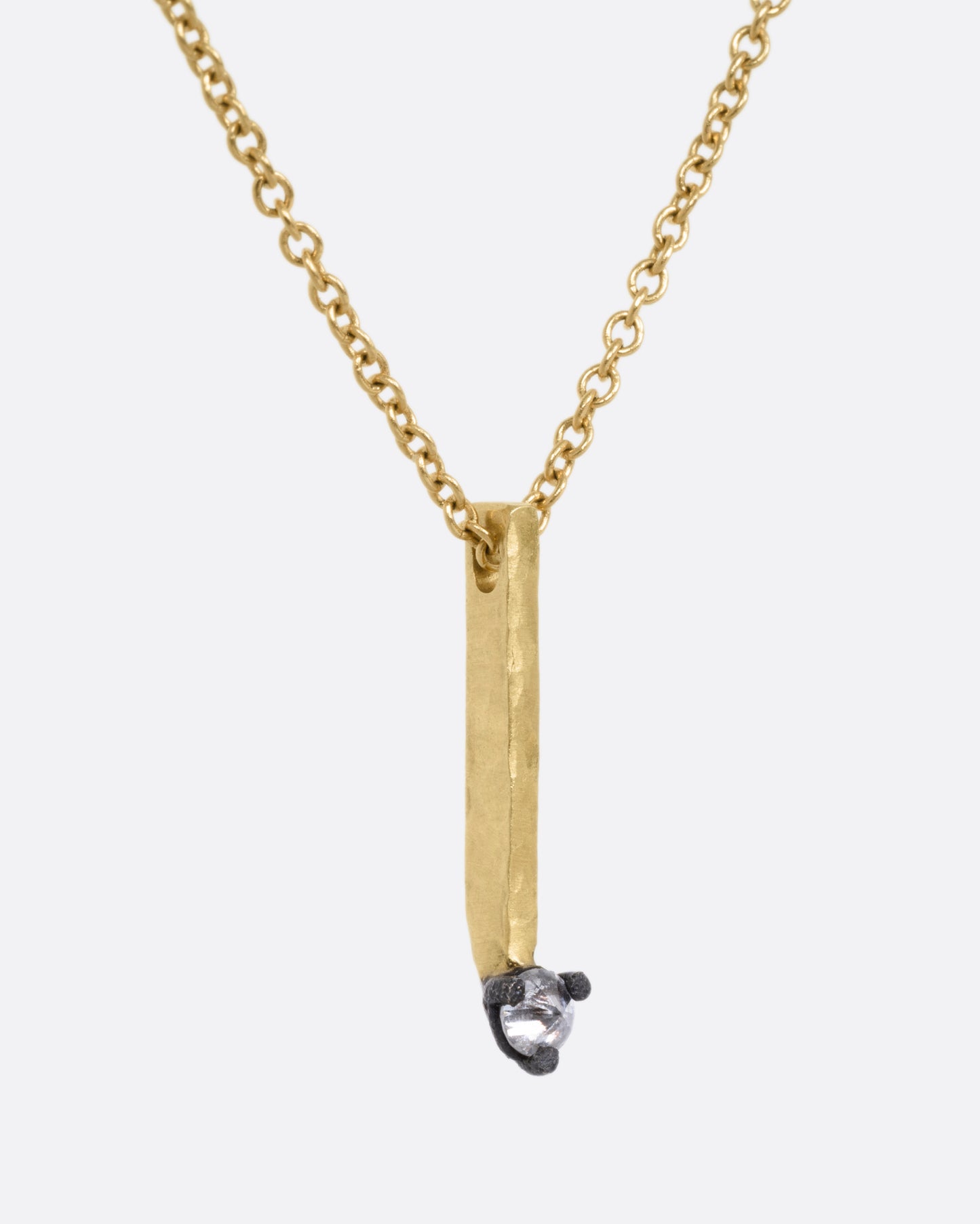 A yellow gold cable chain necklace with a bar pendant studded with an inverted diamond, shown from the side.