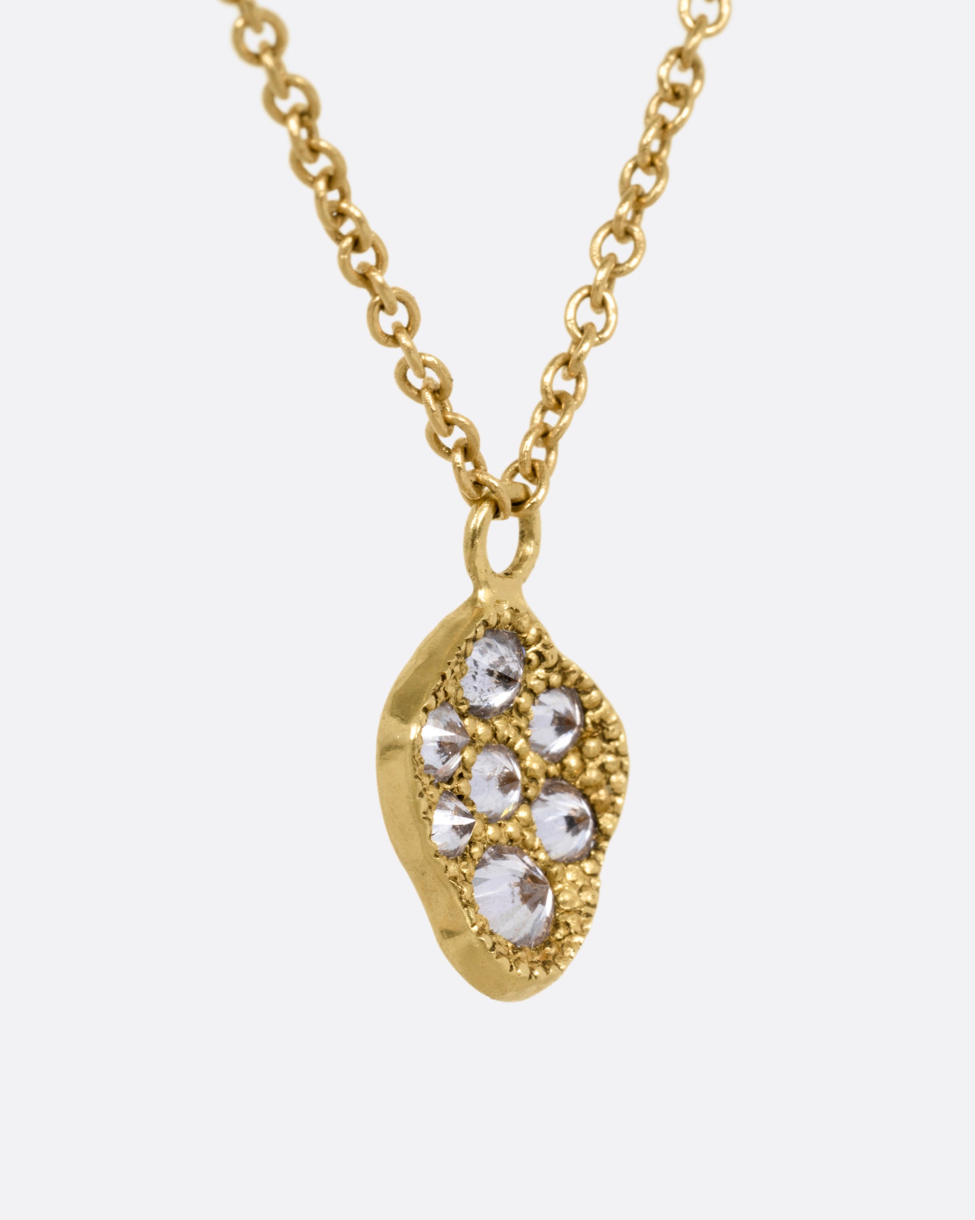 A yellow gold necklace with a concave textured pendant with inverted diamonds. Shown from the side.
