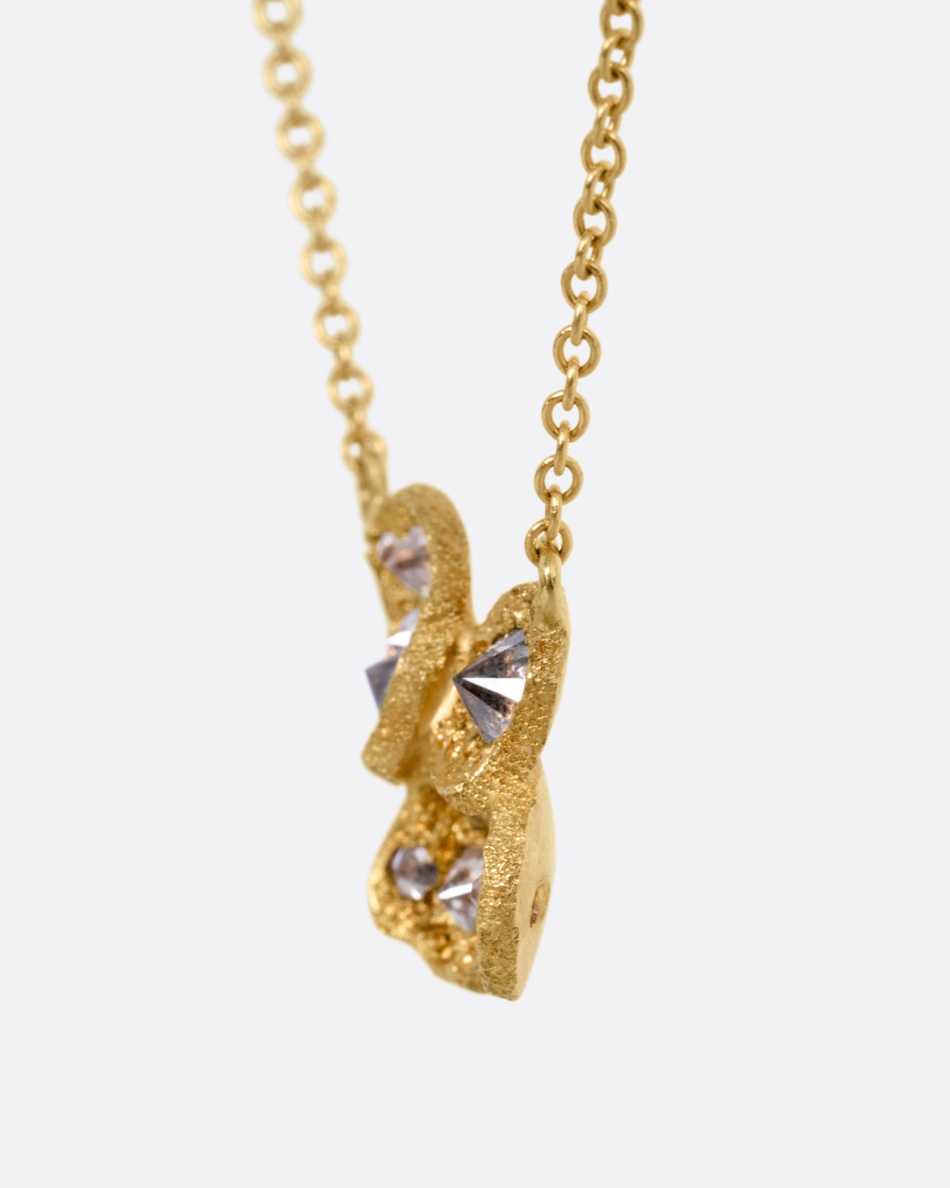 A yellow gold cable chain necklace with a pendant of inverted diamonds in textured divots, shown from the side.