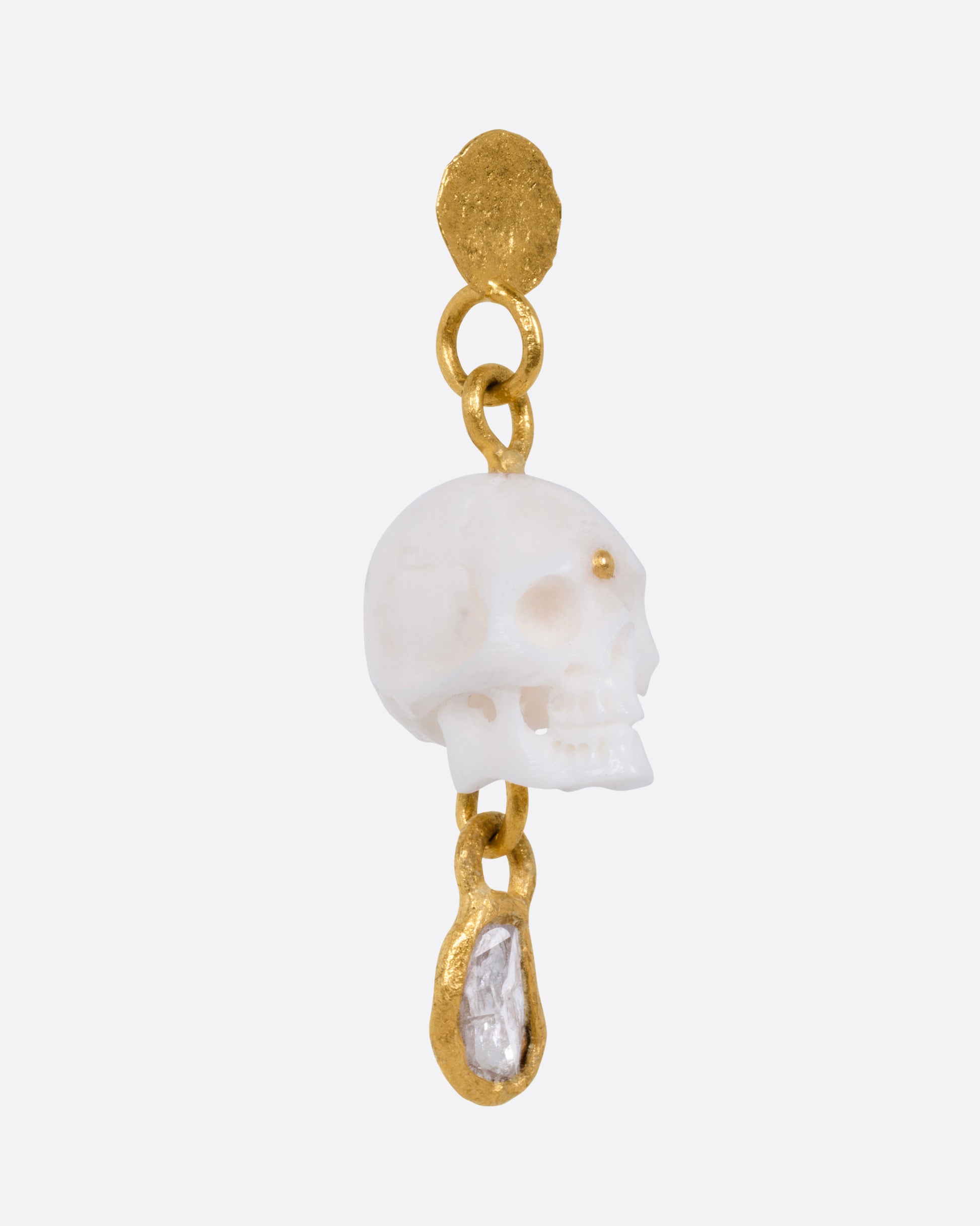 A yellow gold drop stud earring with a carved bone skull and a Borneo diamond, shown from the side.