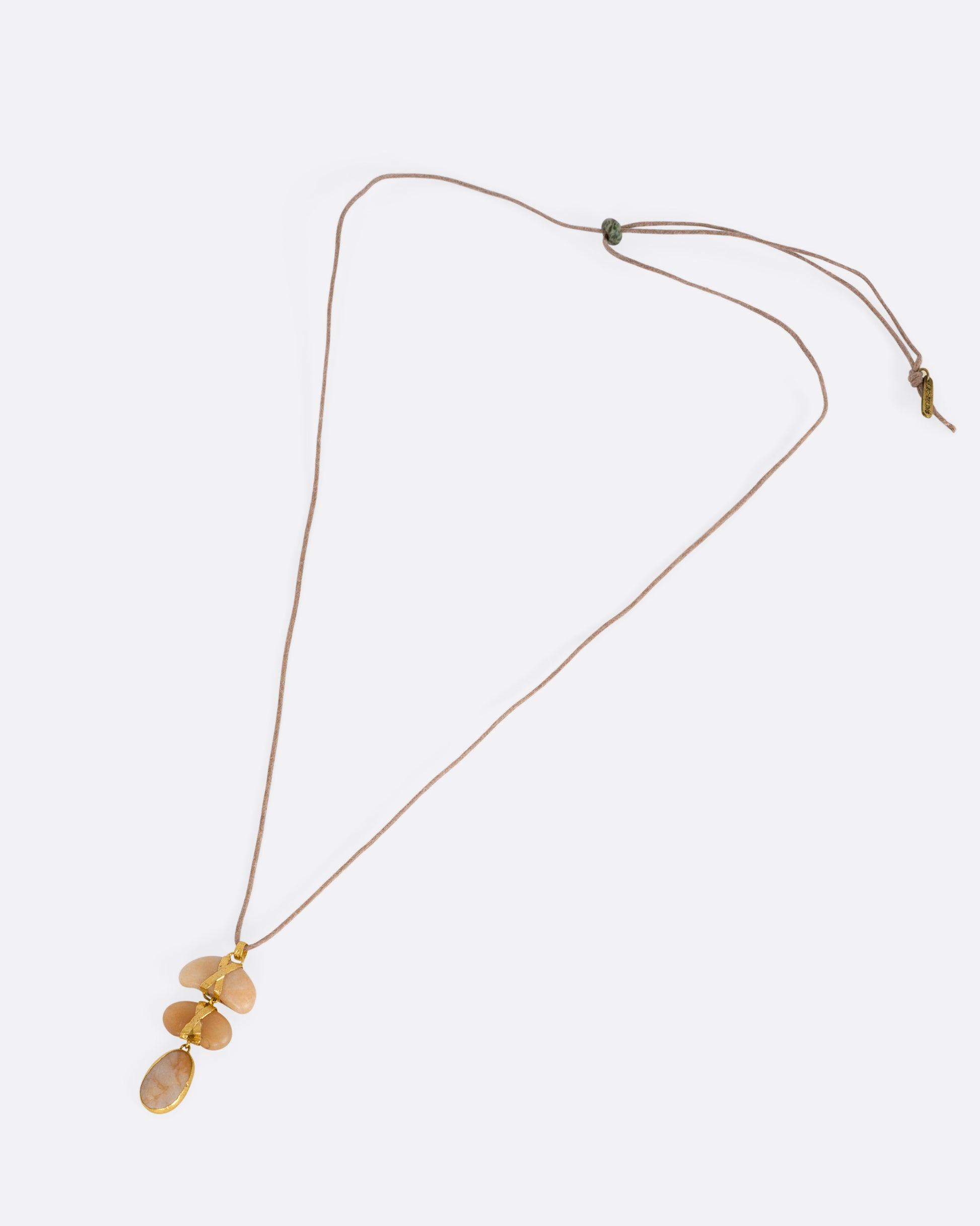 A yellow gold pendant with three  polished pebbles on a cord, shown from the front.