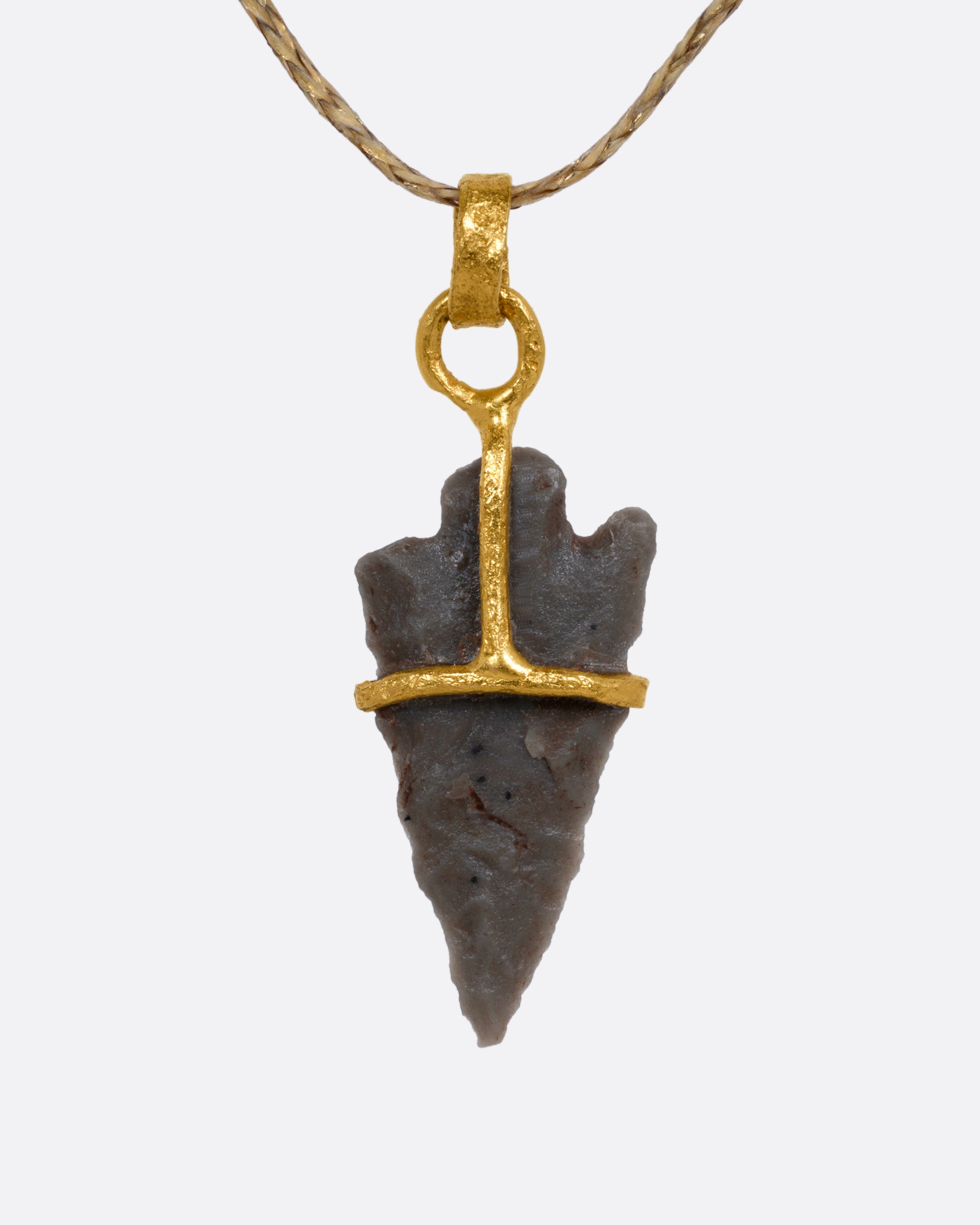 A yellow gold pendant with an ancient arrowhead on a cord, shown from the front.