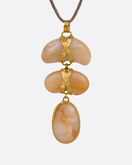 A yellow gold pendant with three  polished pebbles on a cord, shown from the front.