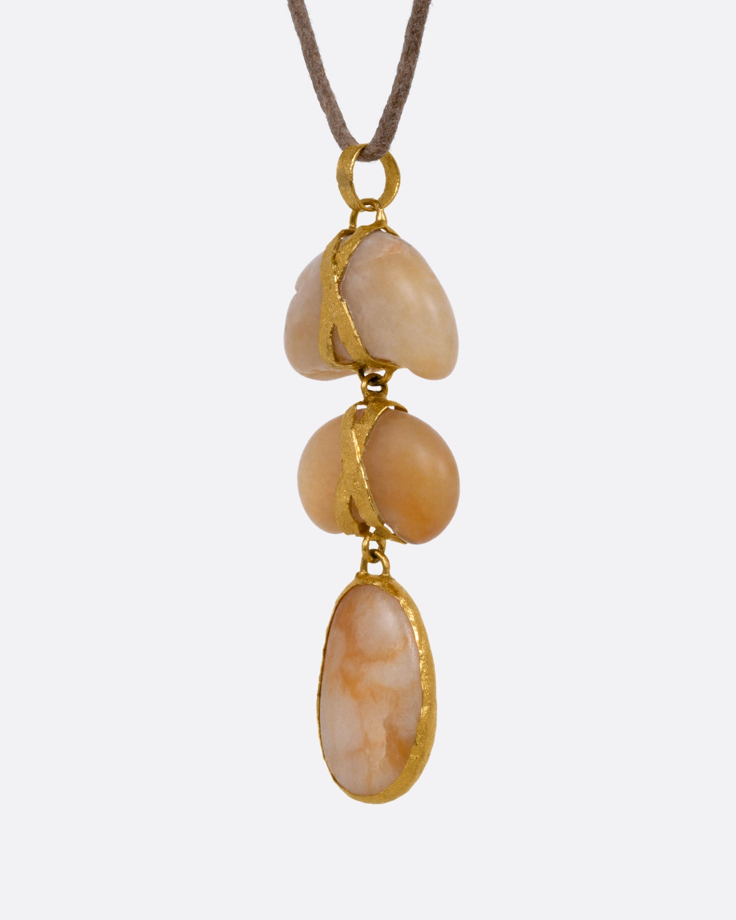 A yellow gold pendant with three  polished pebbles on a cord, shown from the side.