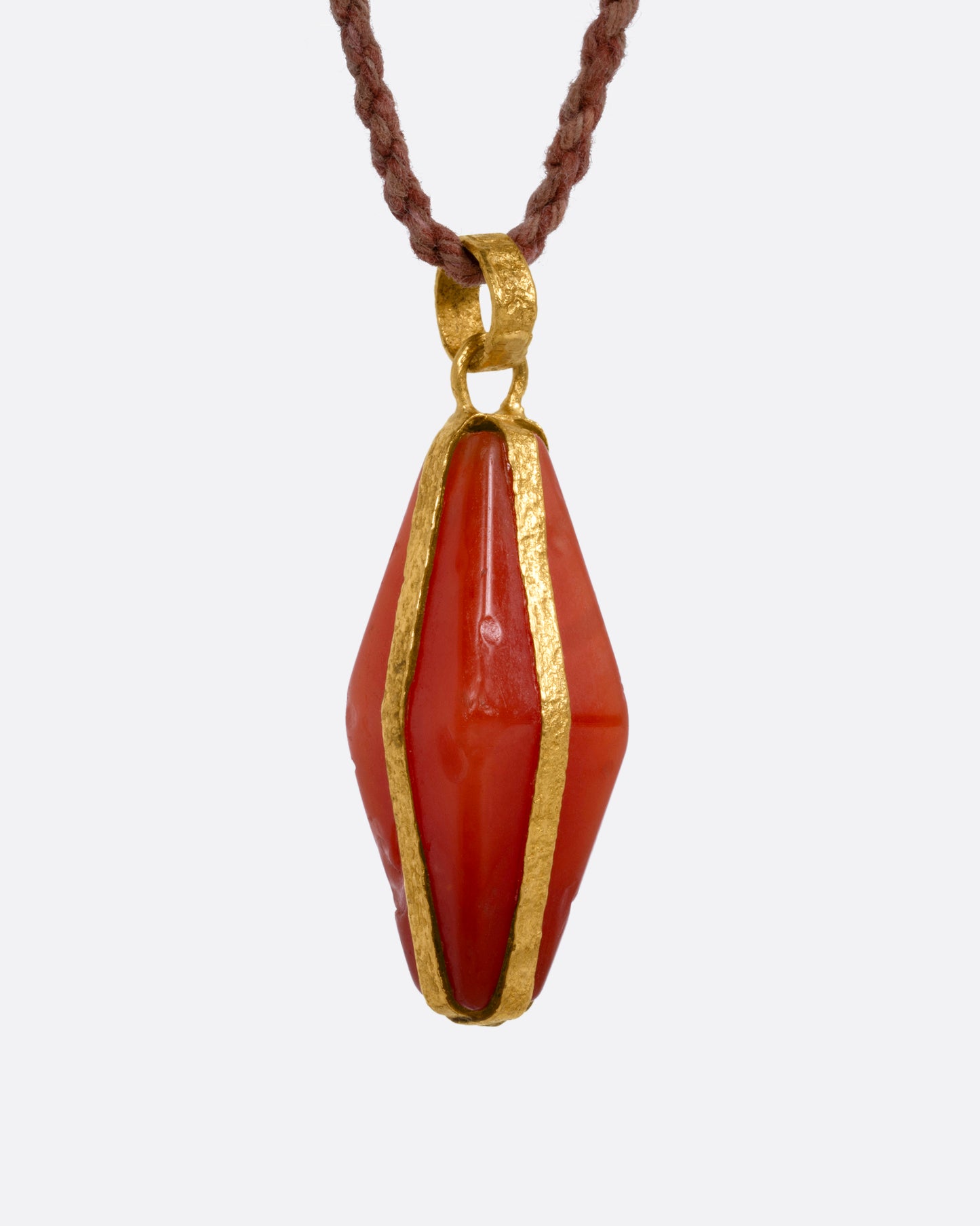 A carnelian pendant wrapped in yellow gold and suspended from a cord, shown from the side. 