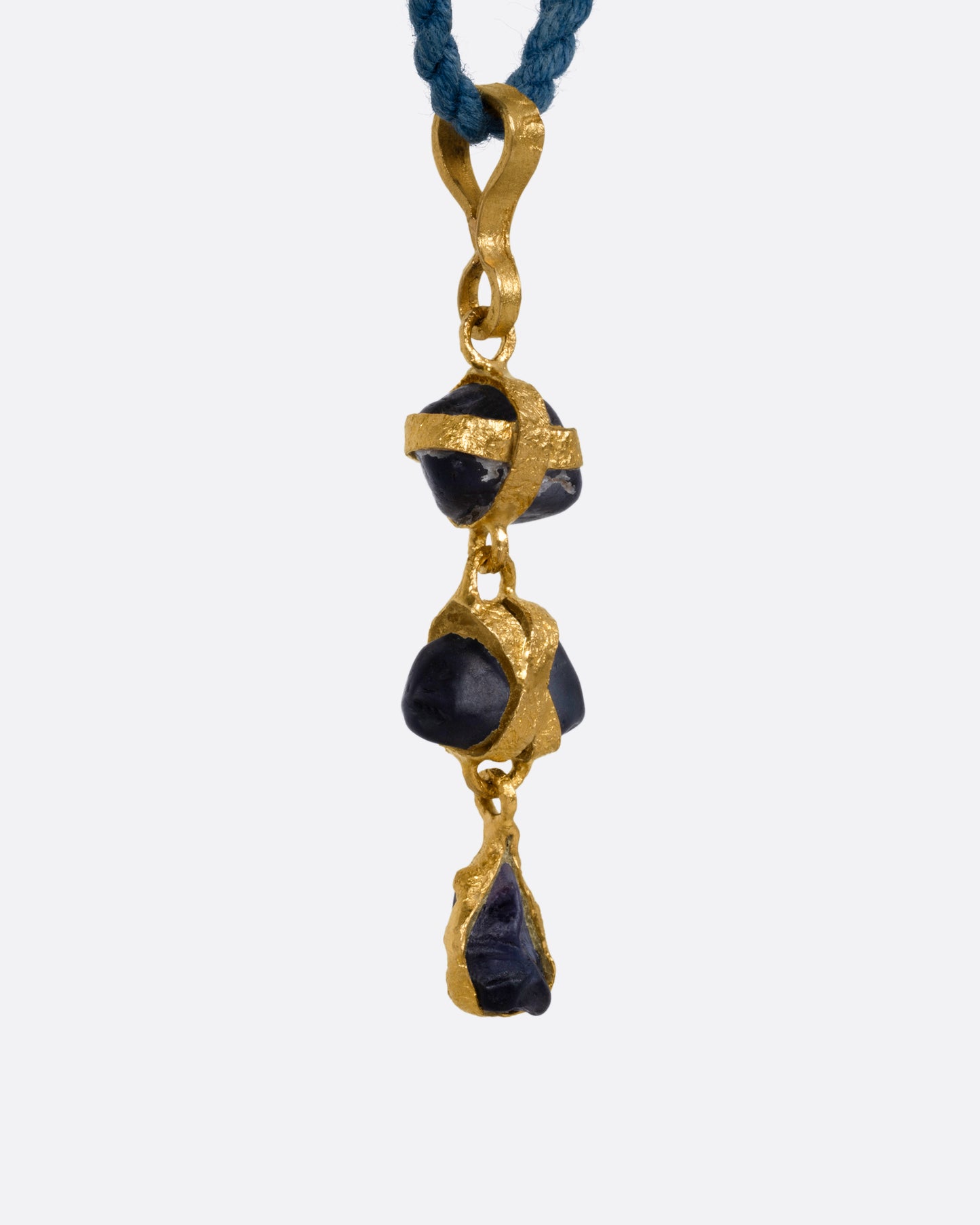 A yellow gold pendant with three  raw sapphires on a cord, shown from the side.