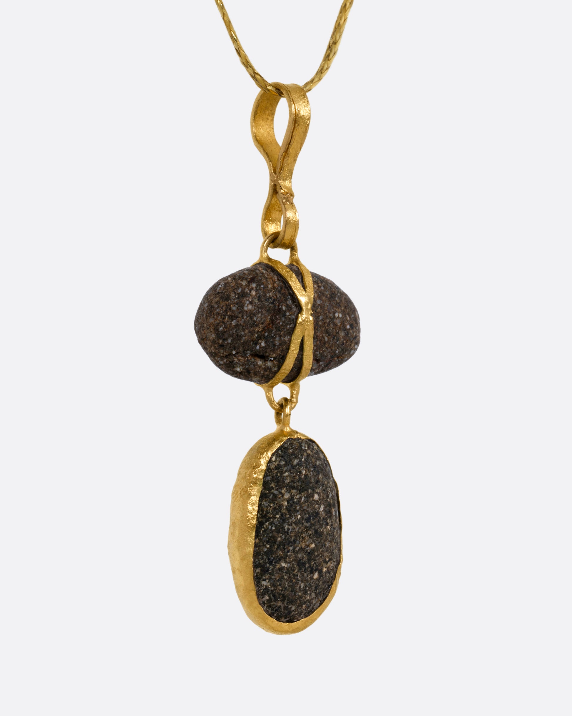 A yellow gold pendant with two Japanese river pebbles on a cord, shown from the side.