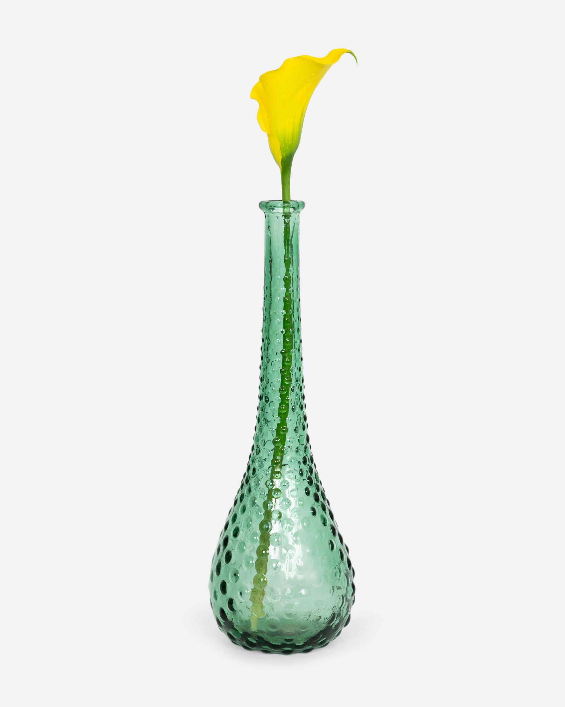 A green glass vase with a raised bubble texture. Shown with a yellow flower.