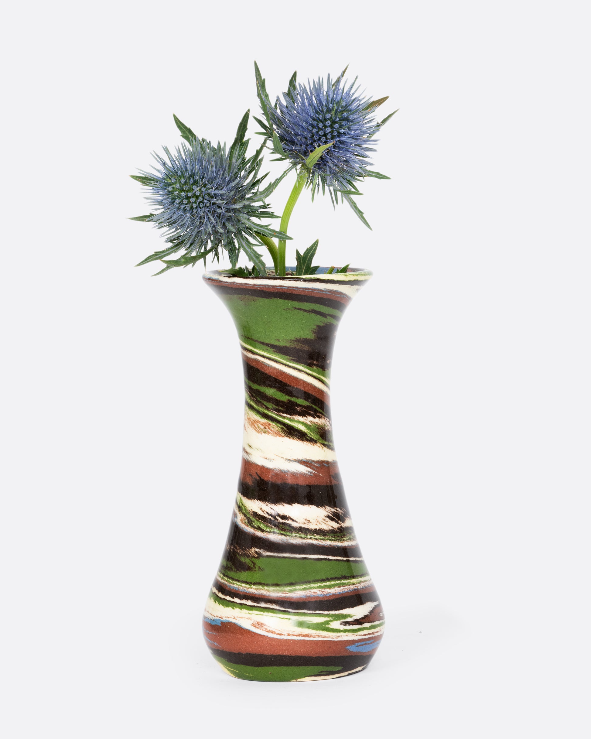A green, brown, and white swirled bud vase. Shown with blue flowers. 