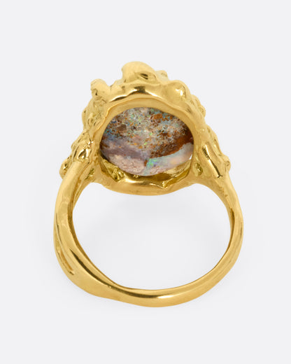 A yellow gold ring with a fossilized wood opal and diamond and emerald accents, shown from the back.
