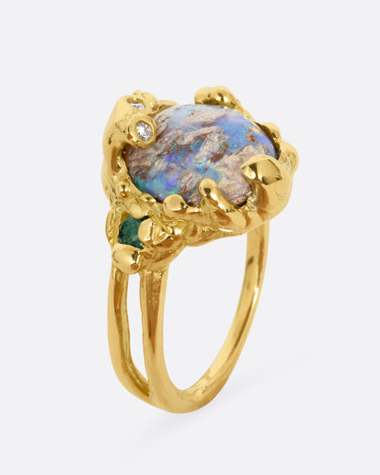 A yellow gold ring with a fossilized wood opal and diamond and emerald accents, shown standing up from the side.