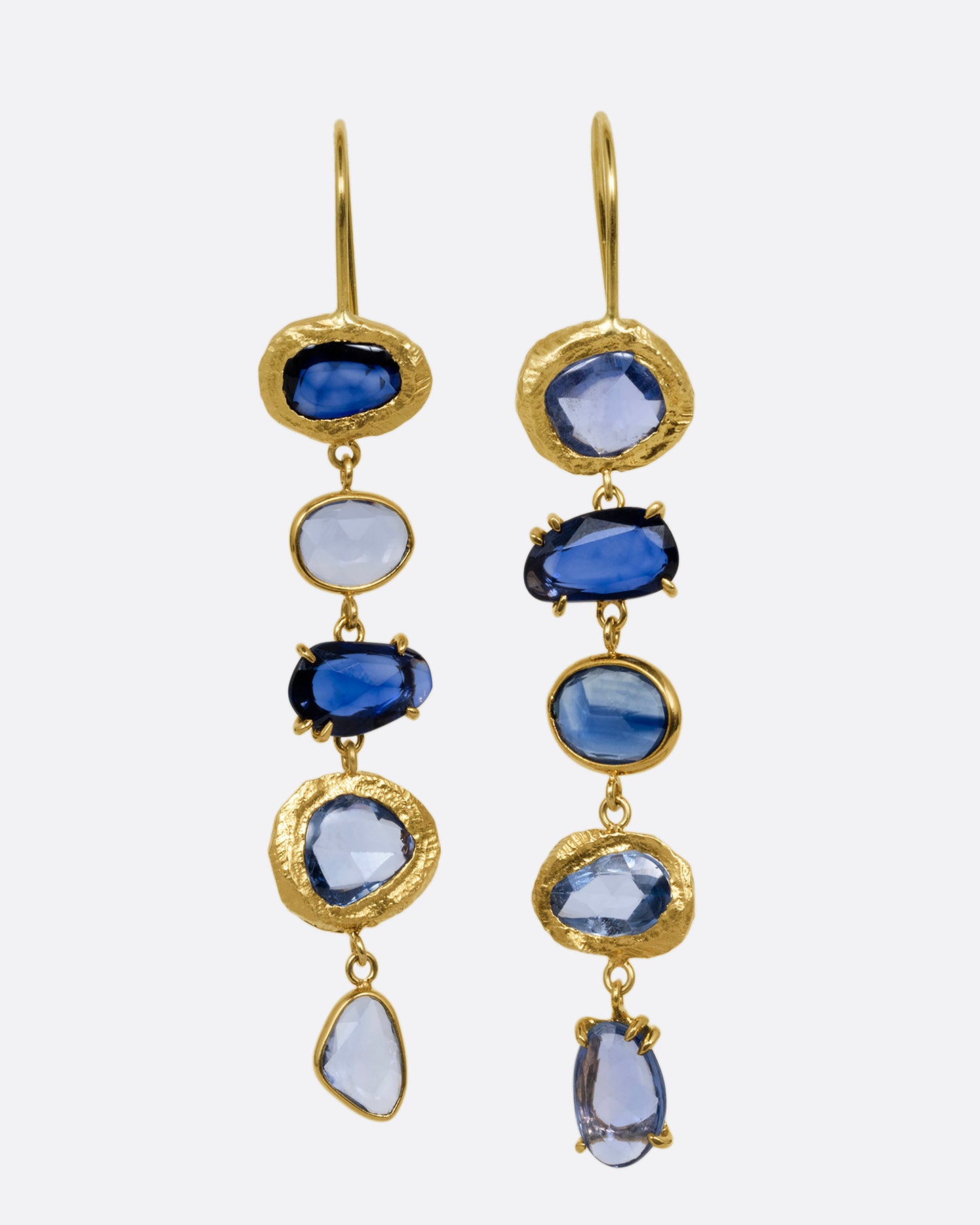A pair of yellow gold dangle earrings with a cascade of blue rose cut sapphires with a mix of hand carved, bezel, and prong settings. Shown from the front.