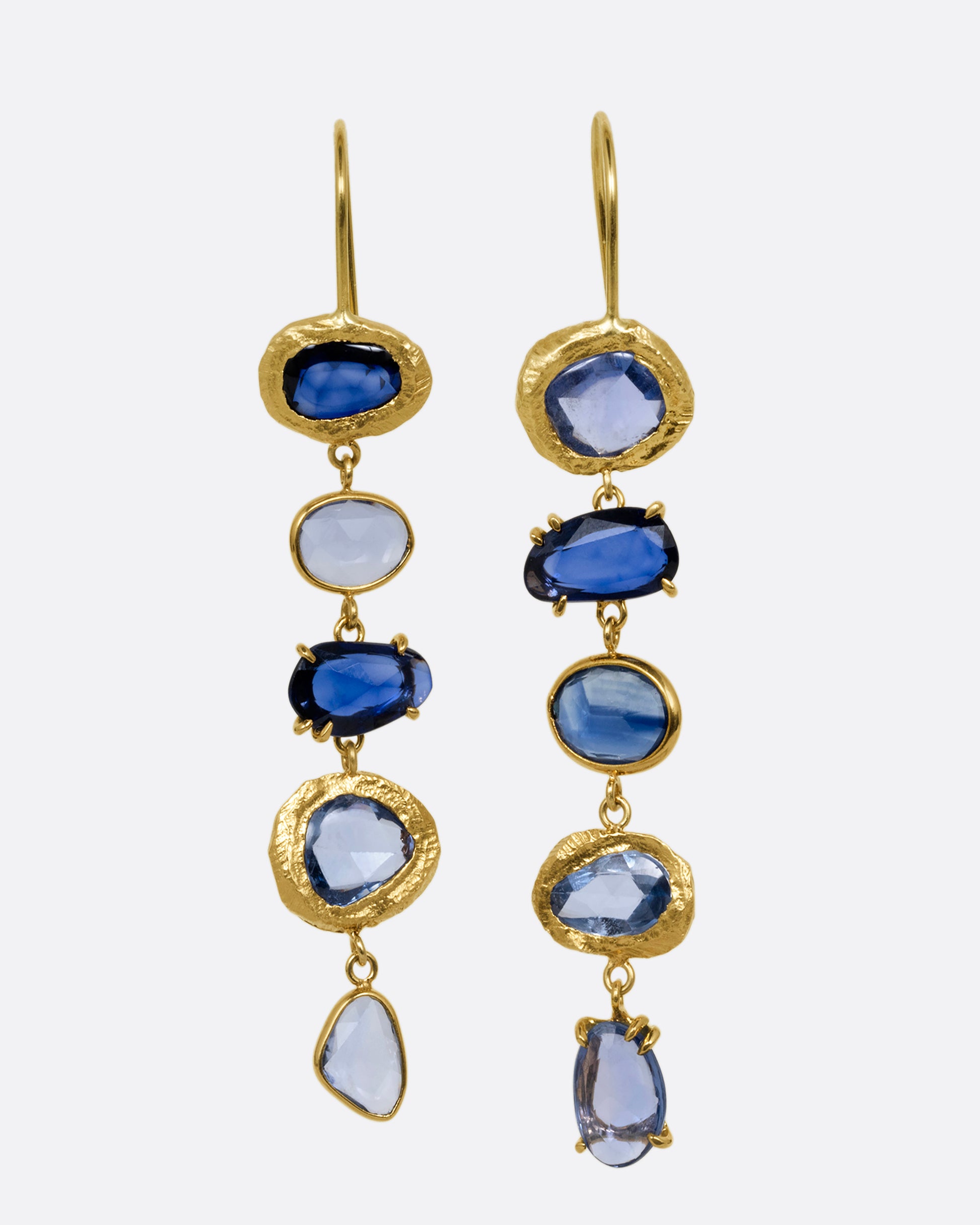 A pair of yellow gold dangle earrings with a cascade of blue rose cut sapphires with a mix of hand carved, bezel, and prong settings. Shown from the front.