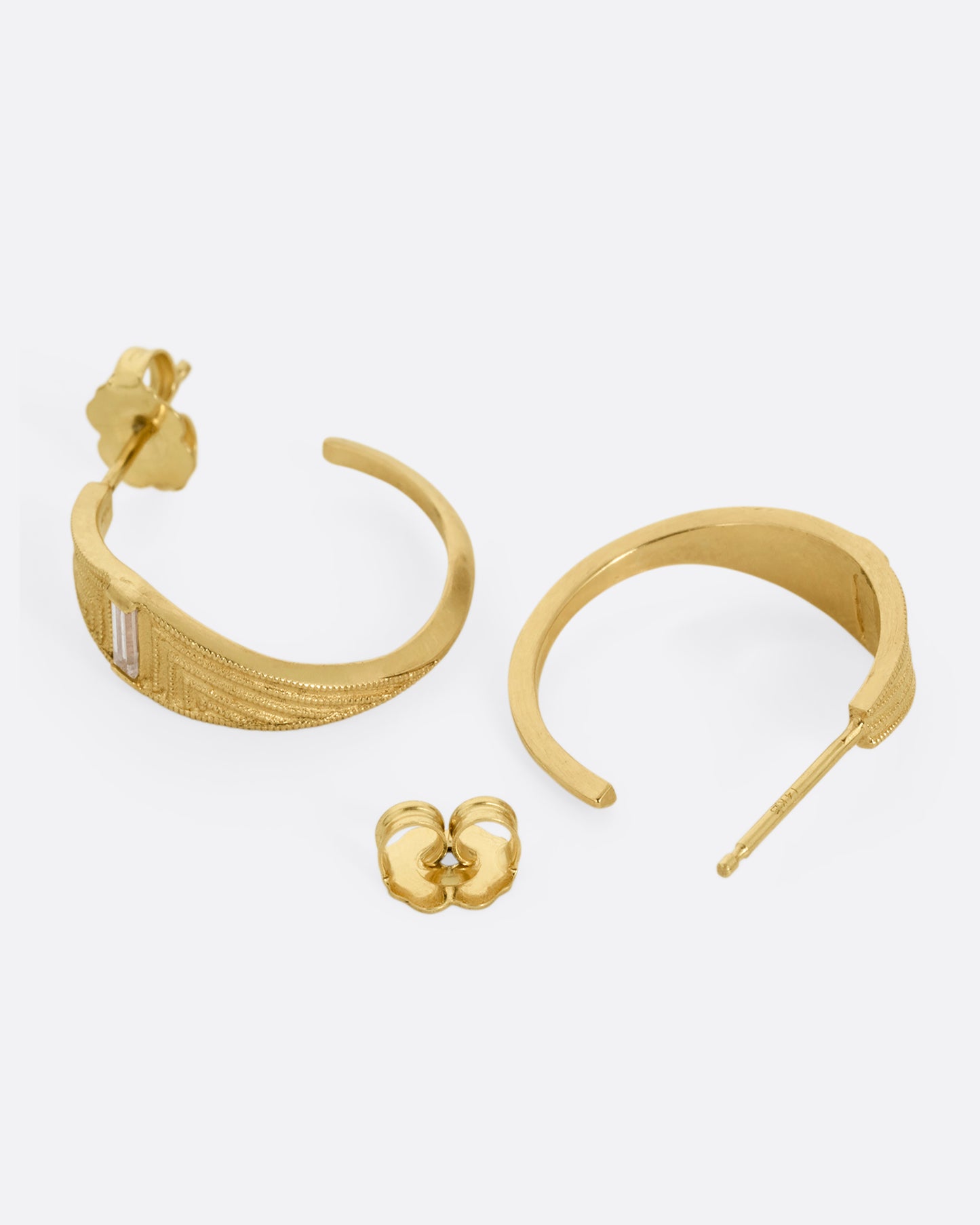 A pair of yellow gold deco inspired hoops with a baguette diamond and a geometric pattern. Shown lying flat; one earring from the front, the other open from the back.