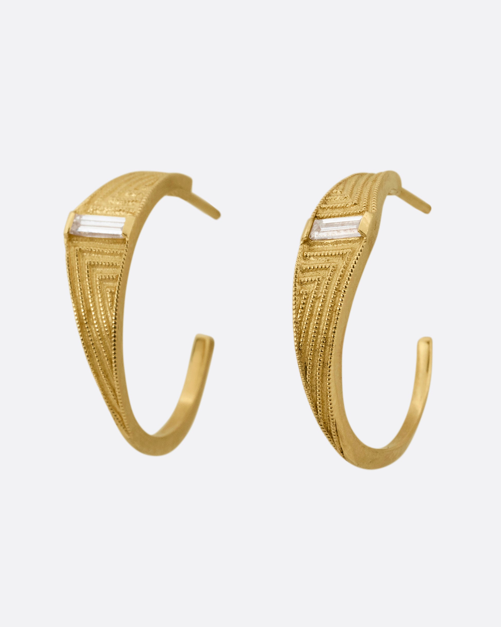 A pair of yellow gold deco inspired hoops with a baguette diamond and a geometric pattern. Shown from the side.