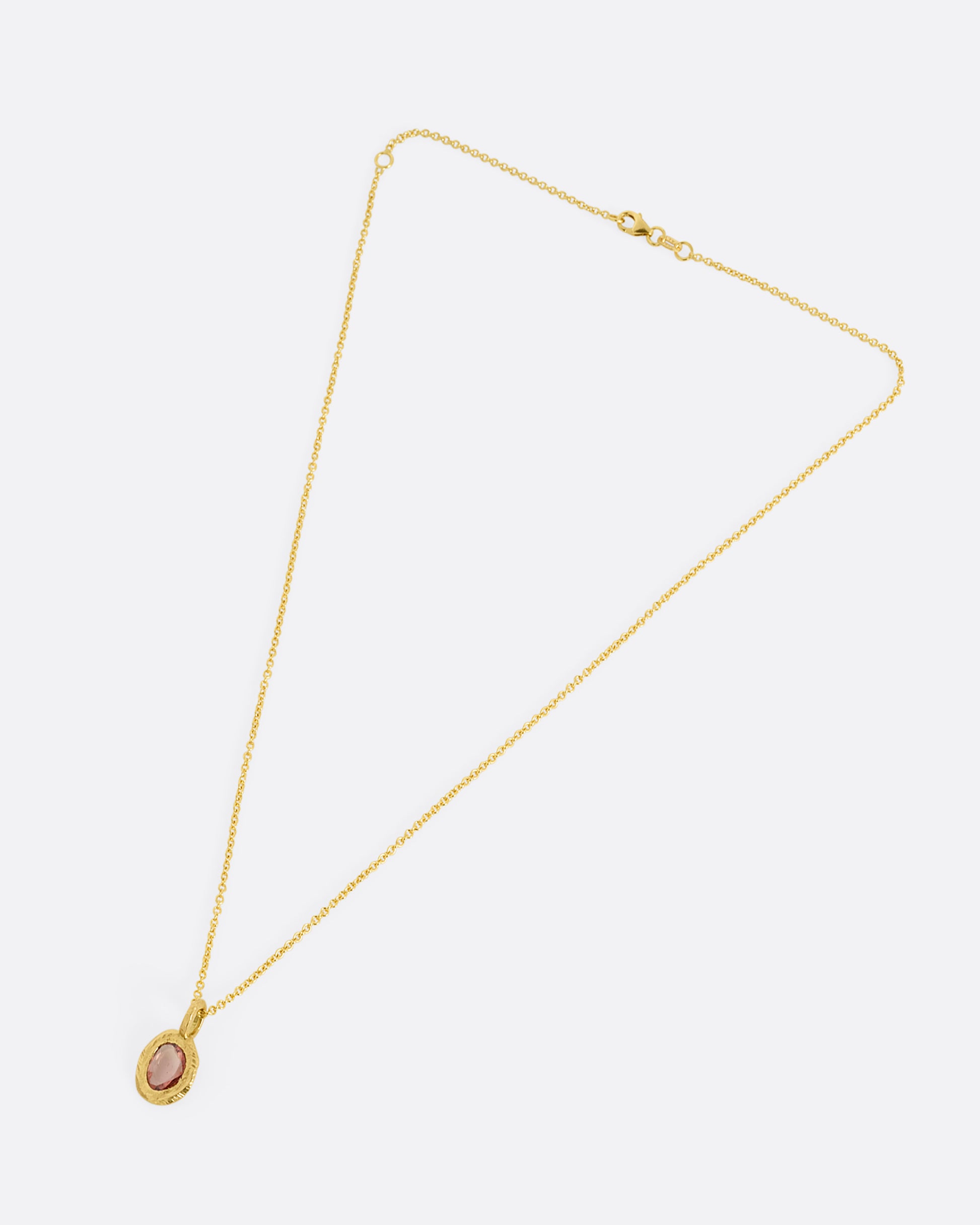 A yellow gold cable chain with a pendant with a burgundy sapphire, shown from the front