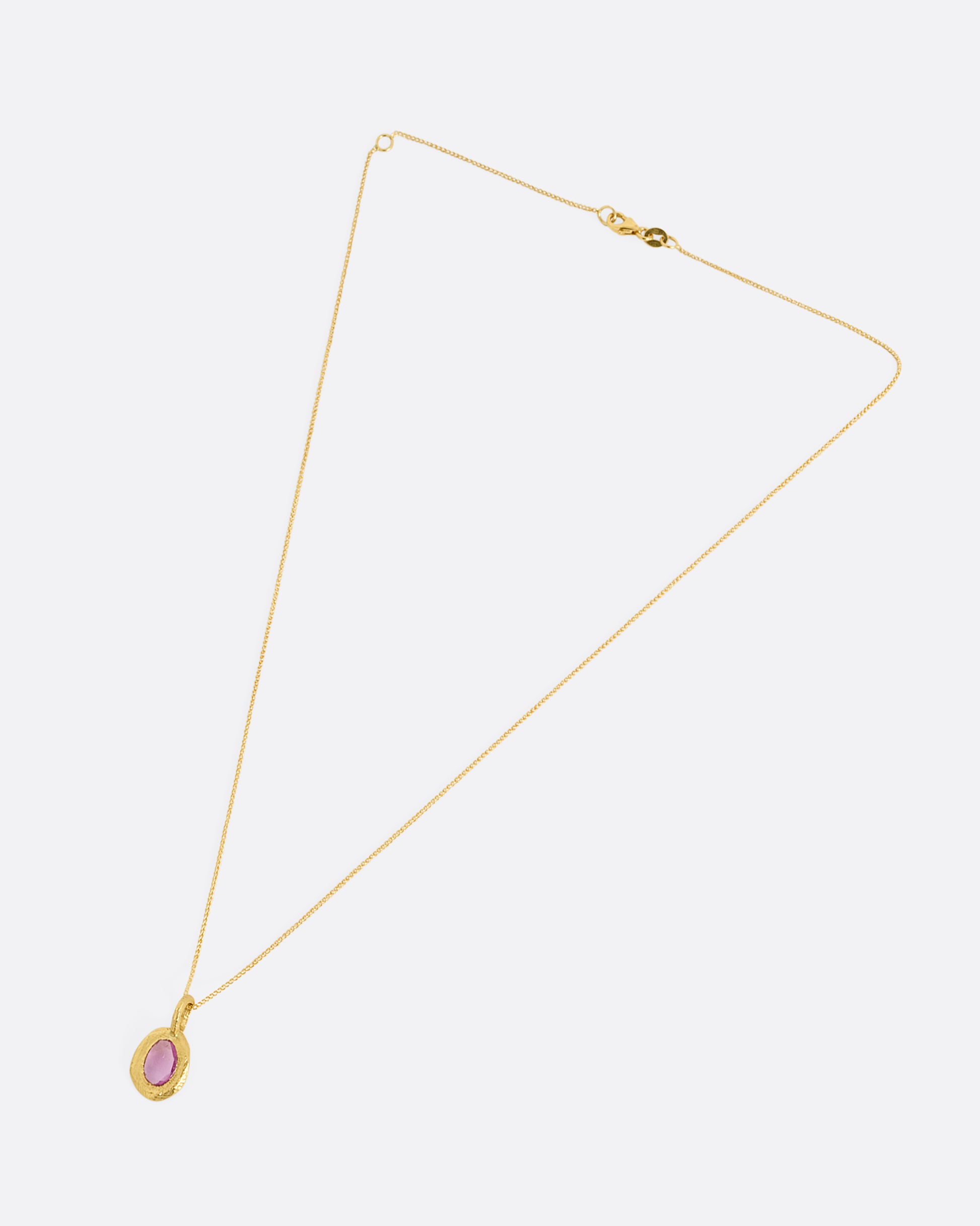 A yellow gold cable chain with a yellow gold pendant with a pink sapphire, shown from the front.