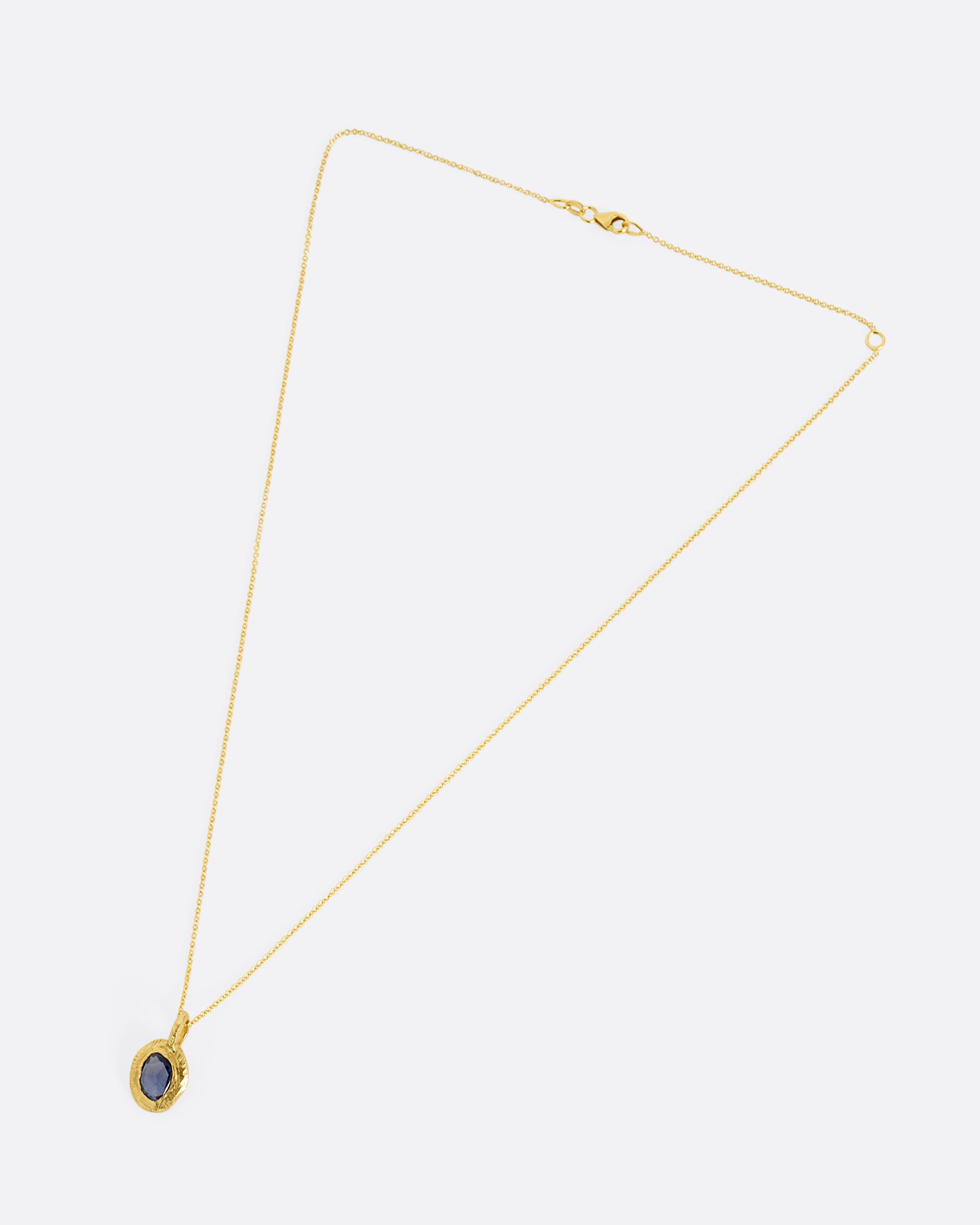 A yellow gold cable chain with a yellow gold pendant with a blue sapphire, shown from the front.