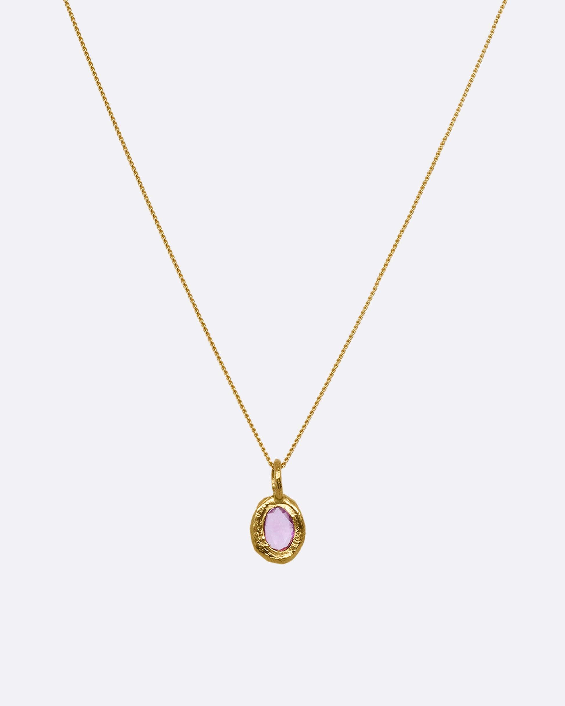 A yellow gold cable chain with a yellow gold pendant with a pink sapphire, shown from the front.
