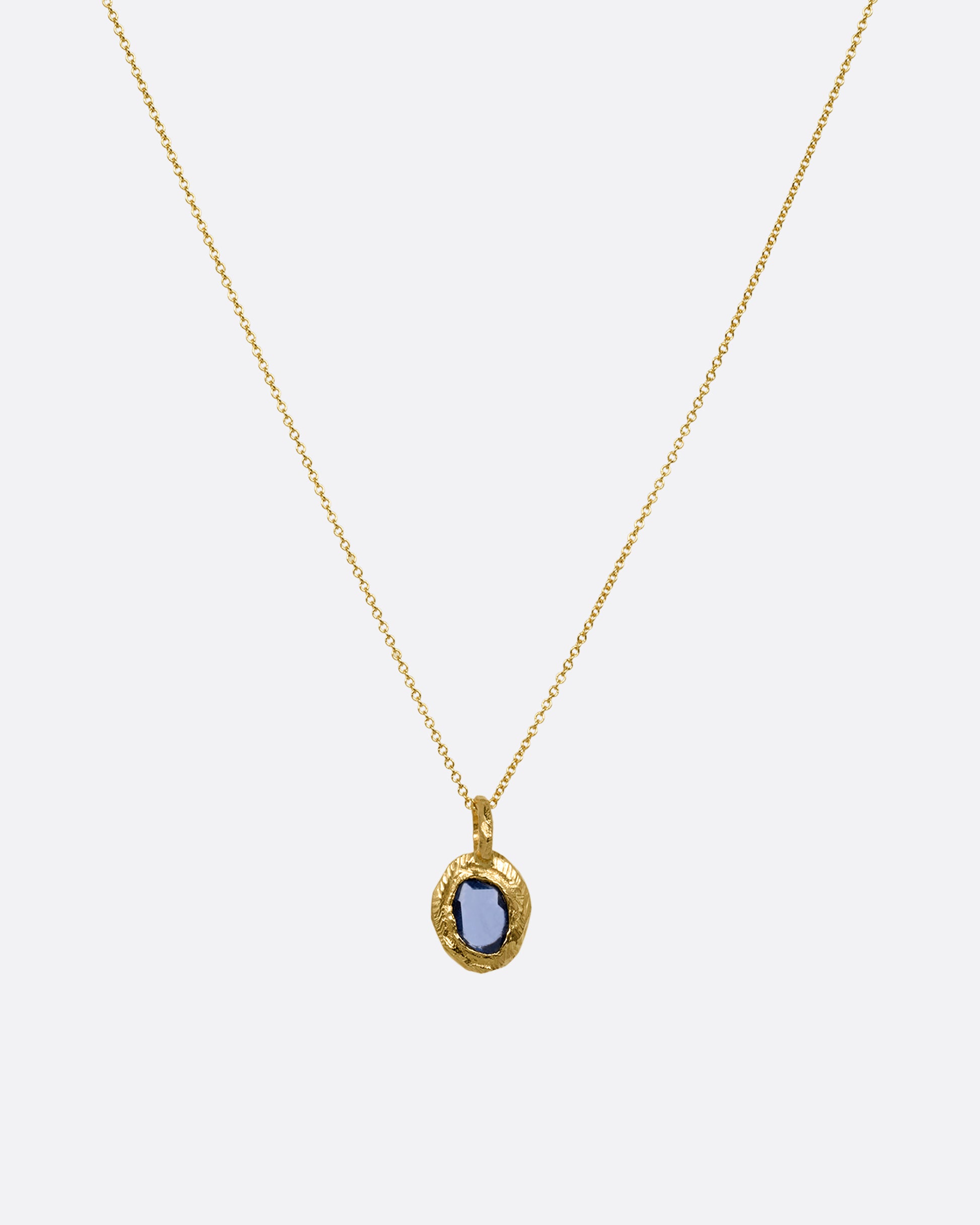 A yellow gold cable chain with a yellow gold pendant with a blue sapphire, shown from the front.