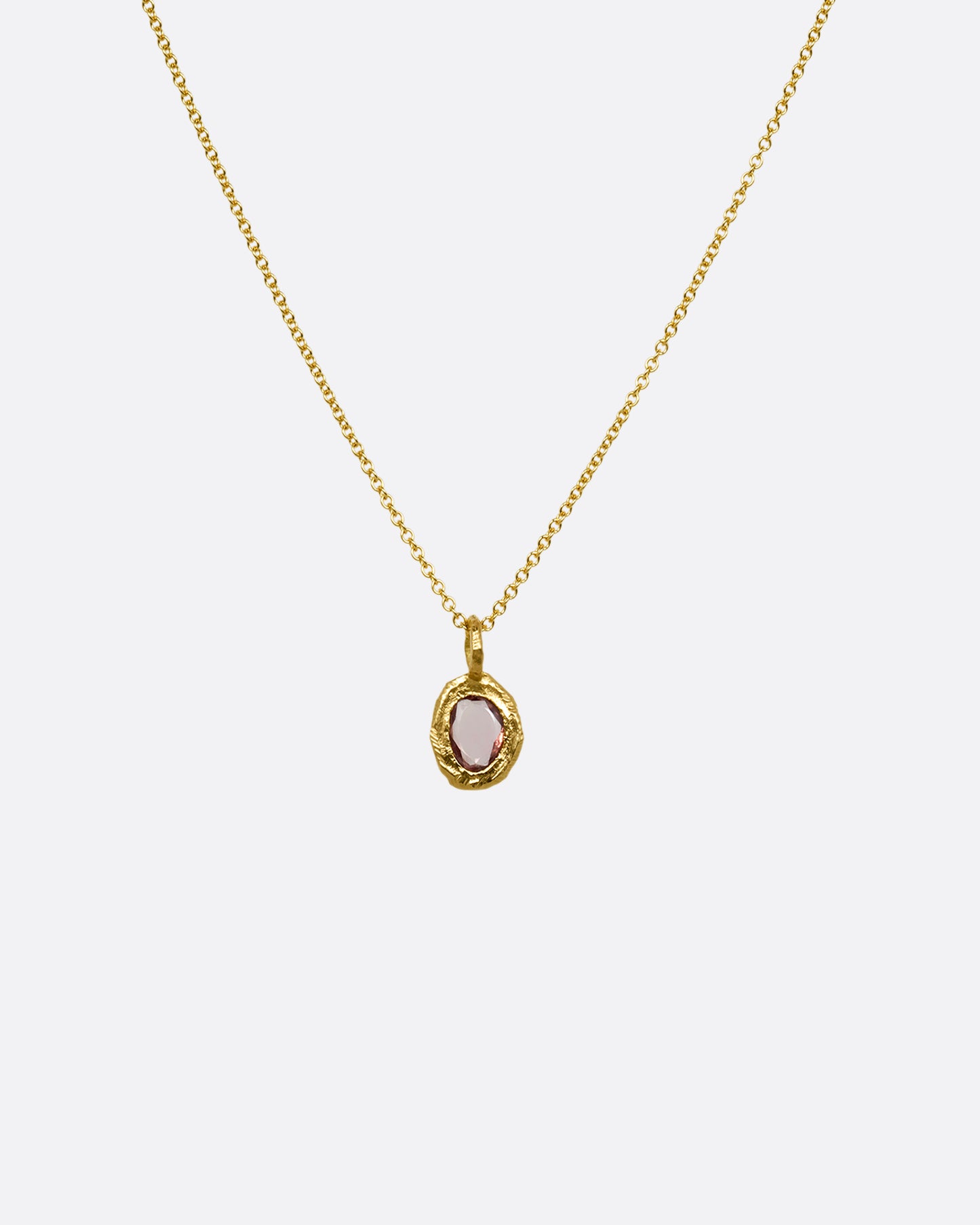 A yellow gold cable chain with a pendant with a burgundy sapphire, shown from the front.