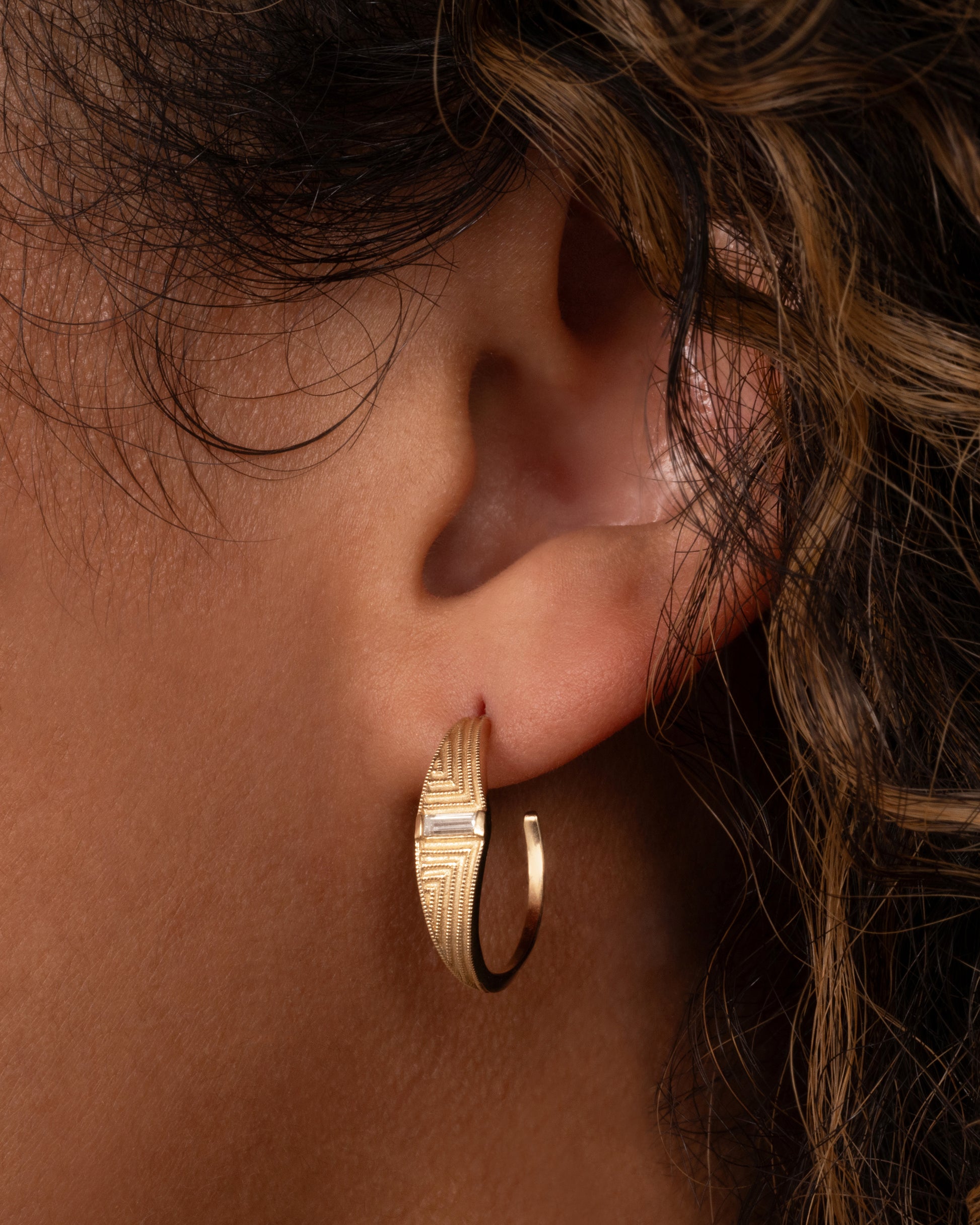 A yellow gold deco inspired hoop with a baguette diamond and a geometric pattern. Shown from the front on a person.