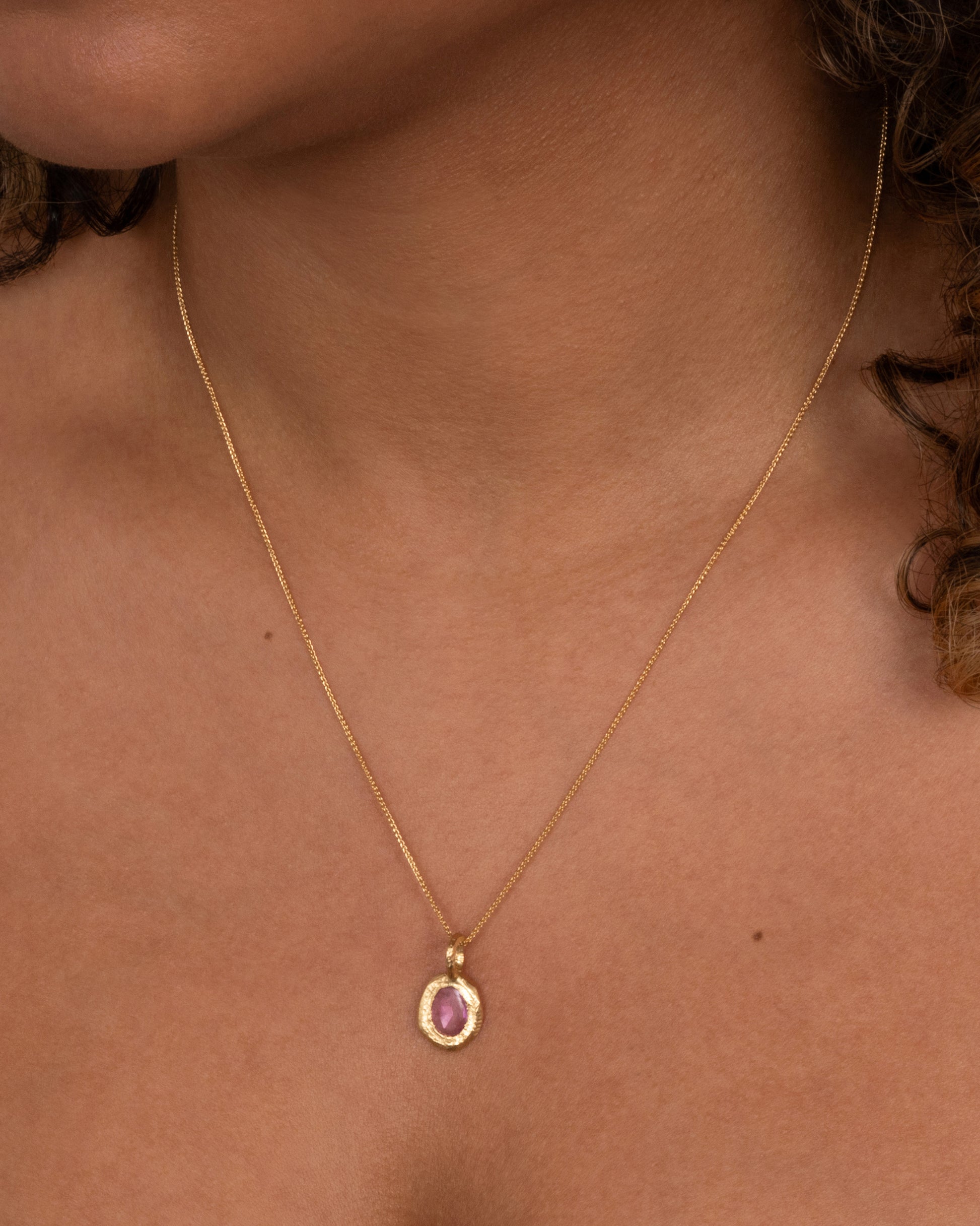 A yellow gold cable chain with a yellow gold pendant with a pink sapphire, shown from the front on a person.