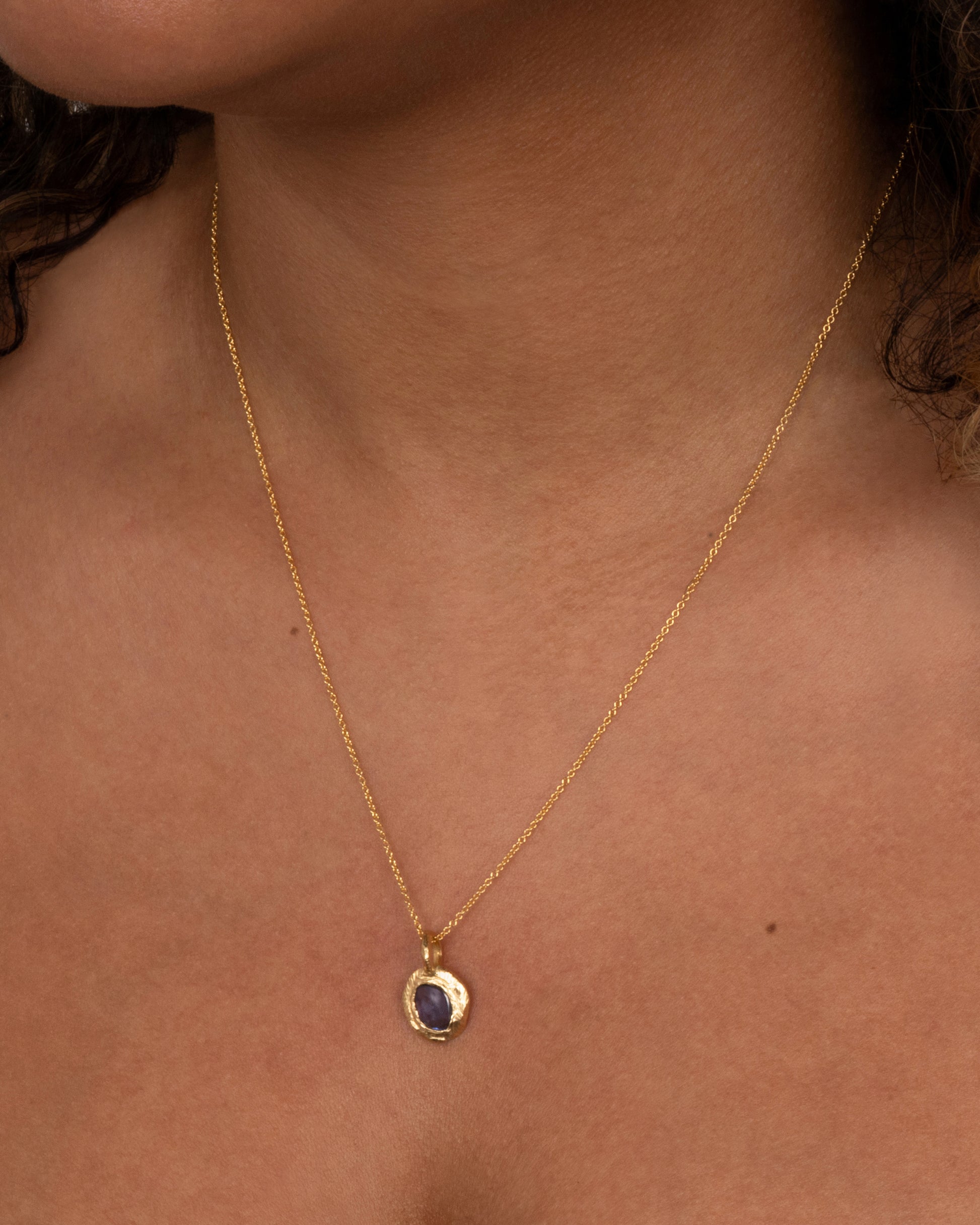 A yellow gold cable chain with a yellow gold pendant with a blue sapphire, shown from the front on a person.