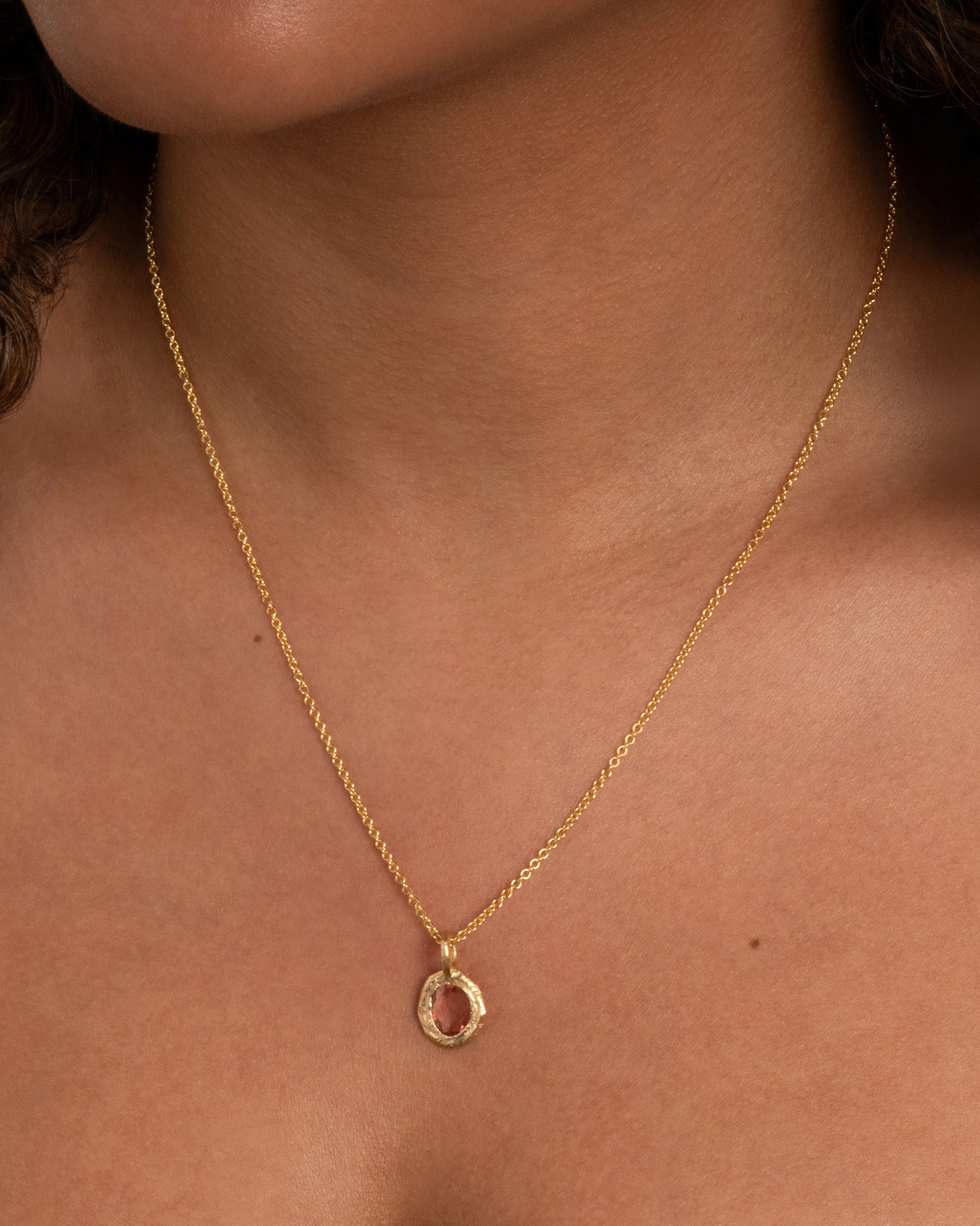 A yellow gold cable chain with a pendant with a burgundy sapphire, shown from the front on a person.