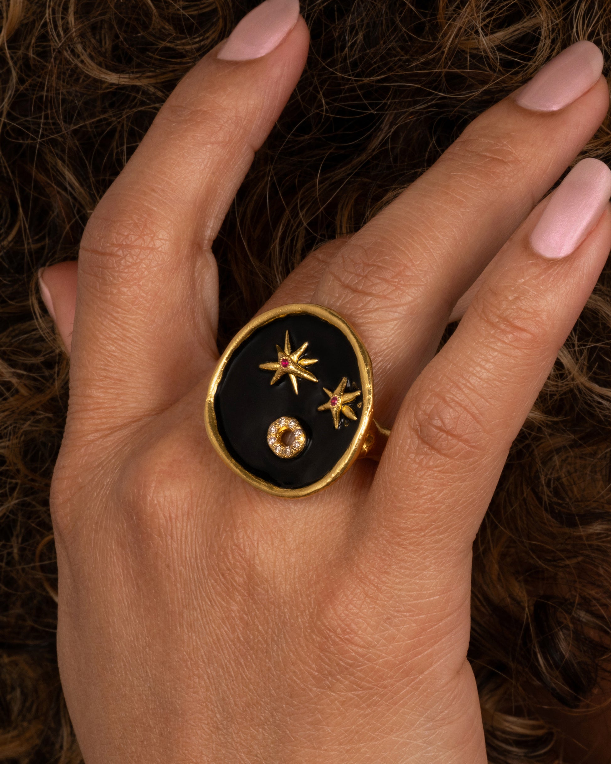 A large high karat gold ring with a round black enamel face, ruby star eyes and a open mouth covered in diamonds. Shown on a finger