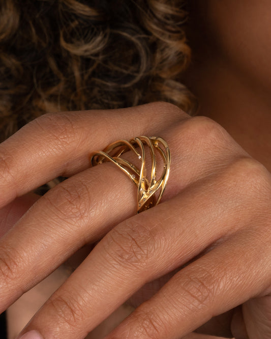 A yellow gold ring formed from multiple strands of gold, dotted with cognac diamonds. Shown on a hand.