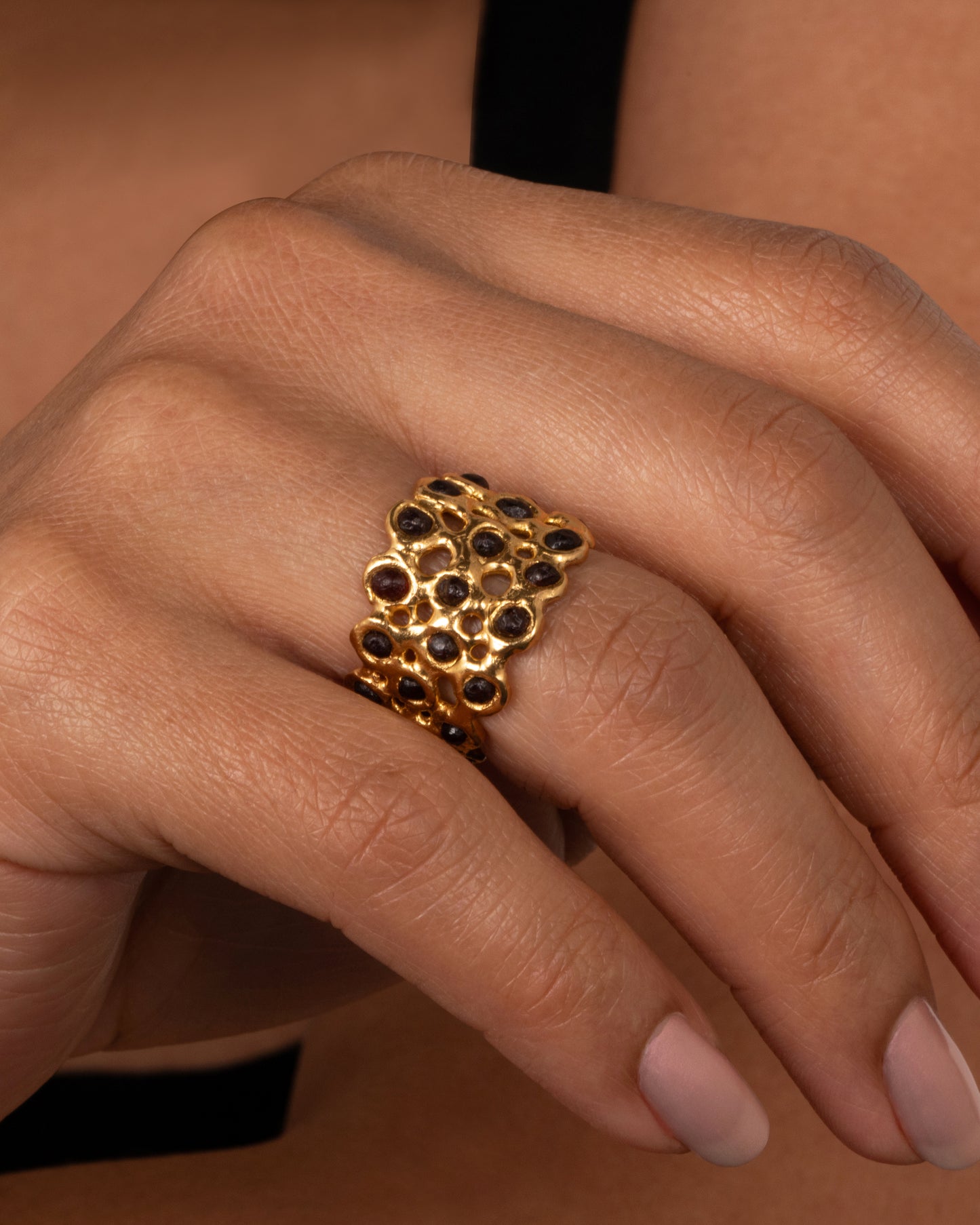 A ring made of a web of dark red garnet nuggets set in high karat gold bezels. Shown on a finger