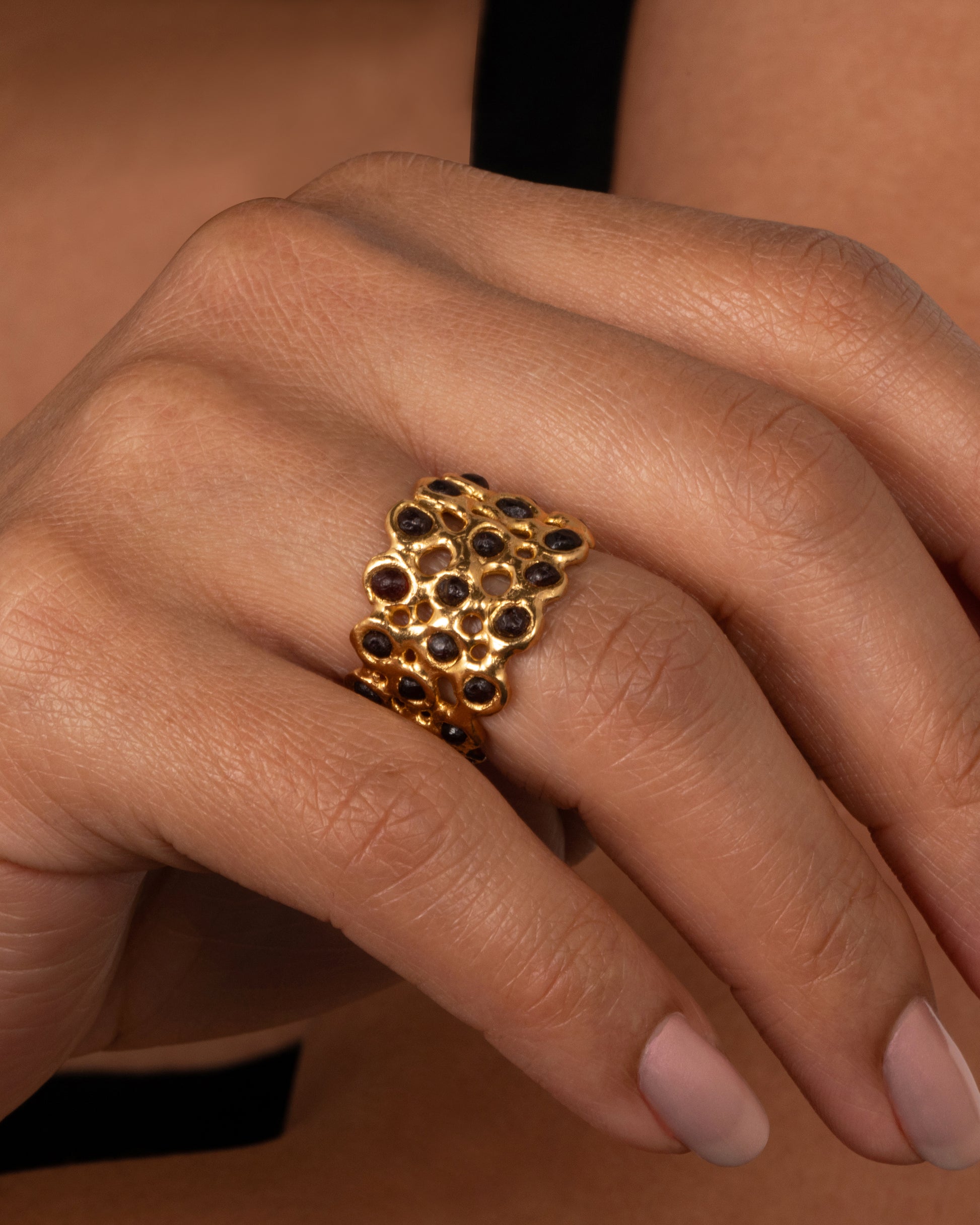 A ring made of a web of dark red garnet nuggets set in high karat gold bezels. Shown on a finger
