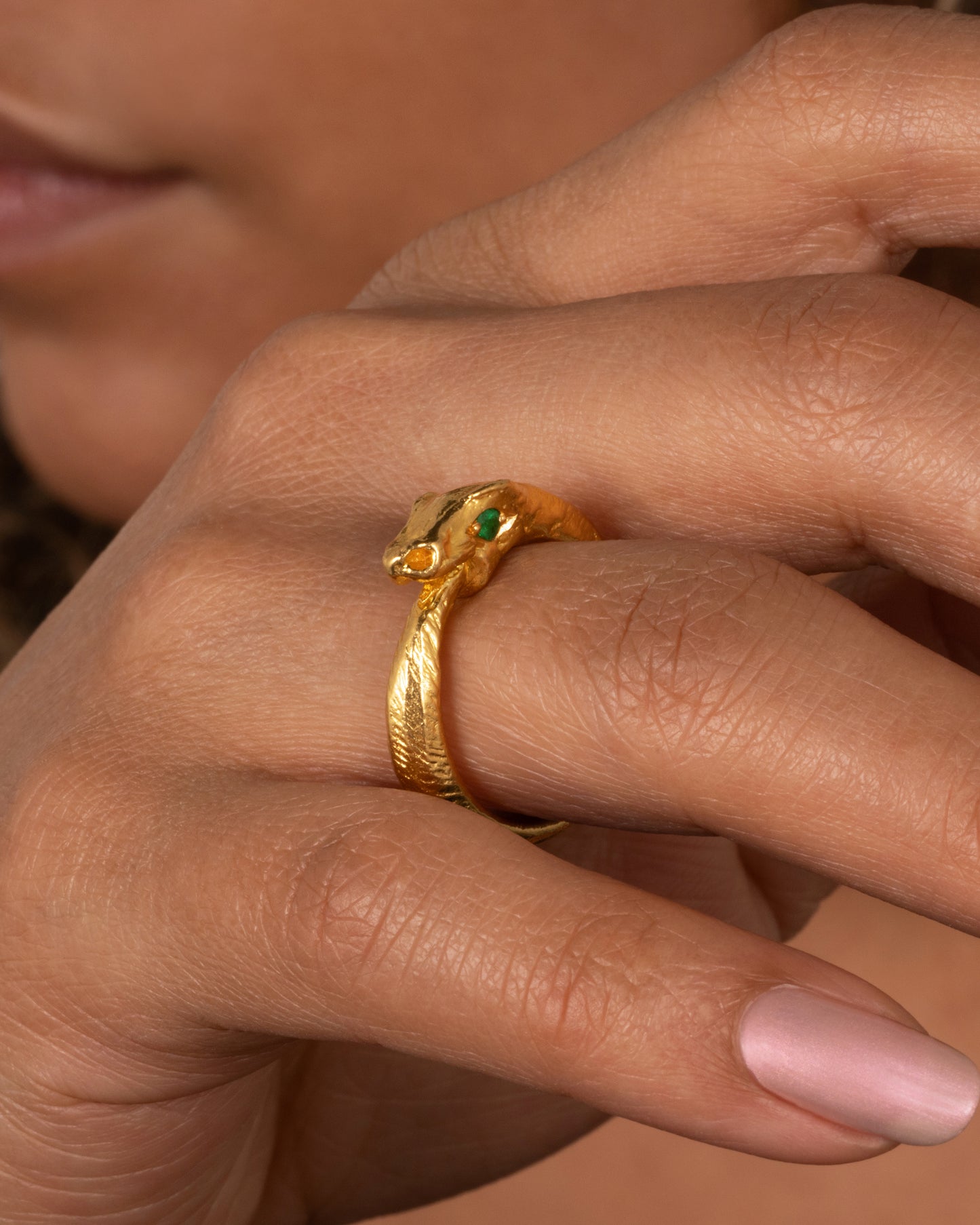 A high karat gold ouroboros ring showing a serpent catching its own tail. Shown on a finger.