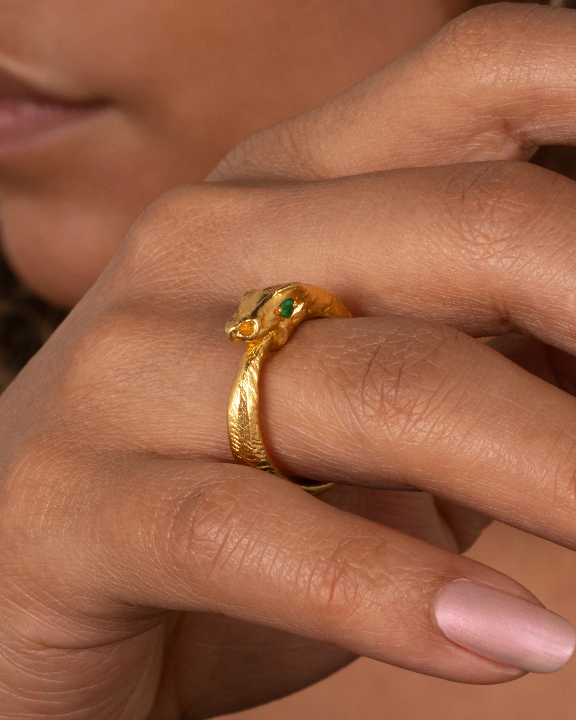 A high karat gold ouroboros ring showing a serpent catching its own tail. Shown on a finger.