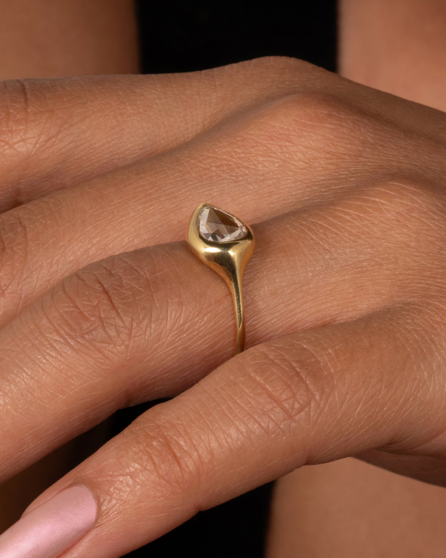 A yellow gold band with a rose cut pear shaped diamond. Shown worn on a finger.
