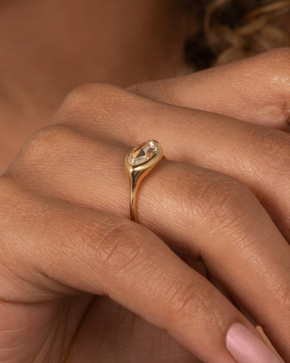 A yellow gold ring with a horizontal rose cut marquise diamond. Shown on a finger.
