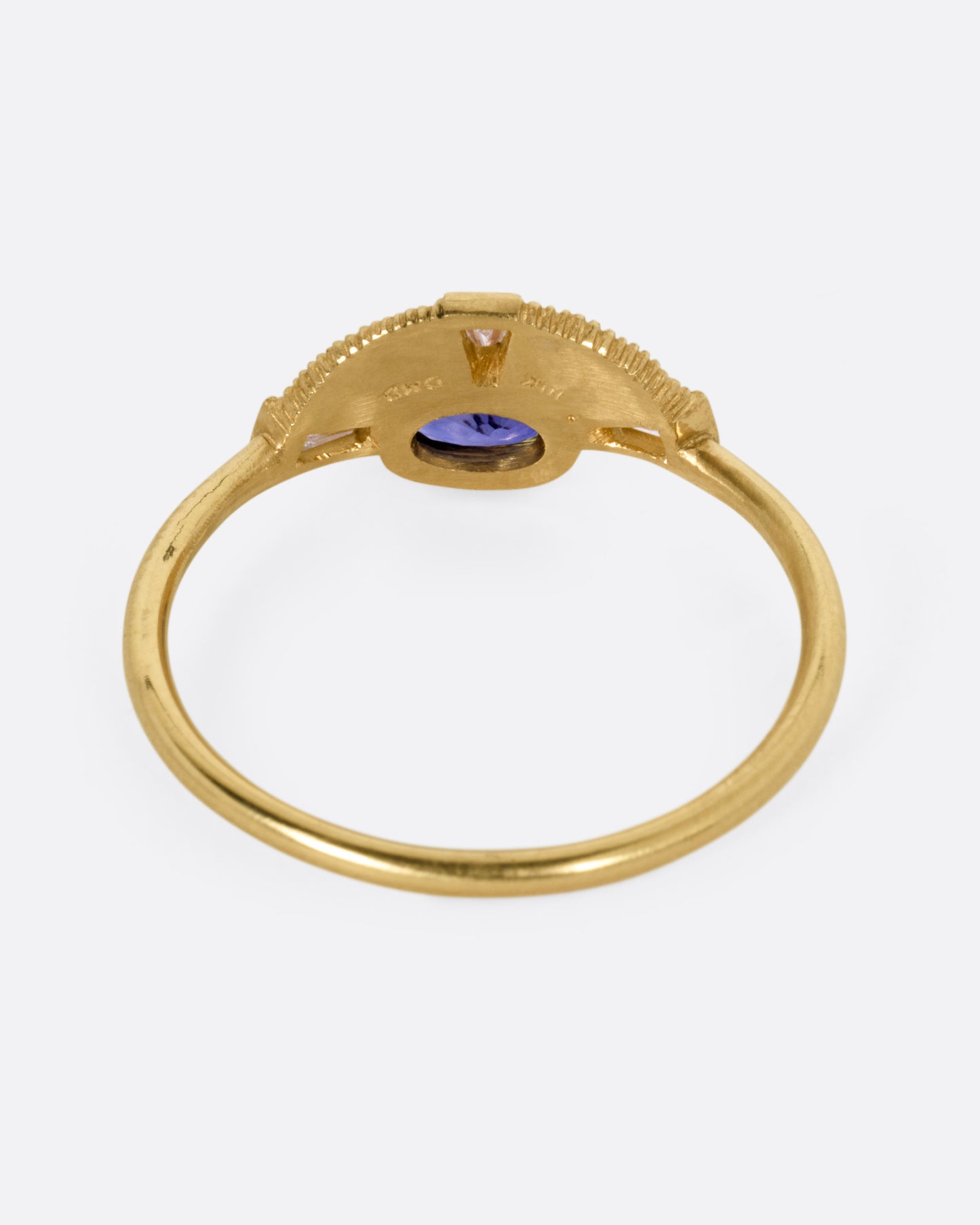 A yellow gold ring with a purple sapphire and three baguette diamonds, shown from the back.