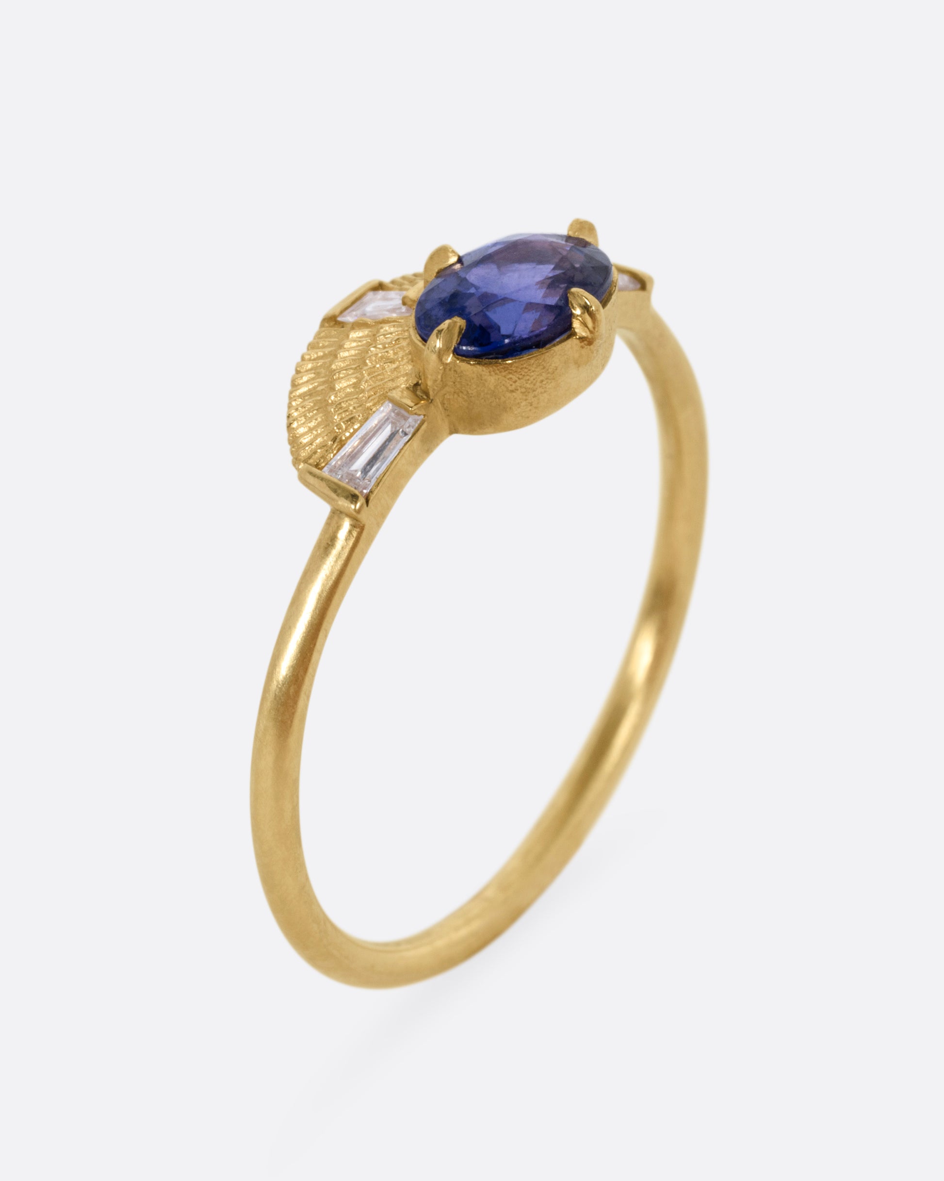 A yellow gold ring with a purple sapphire and three baguette diamonds, shown from the side standing up.