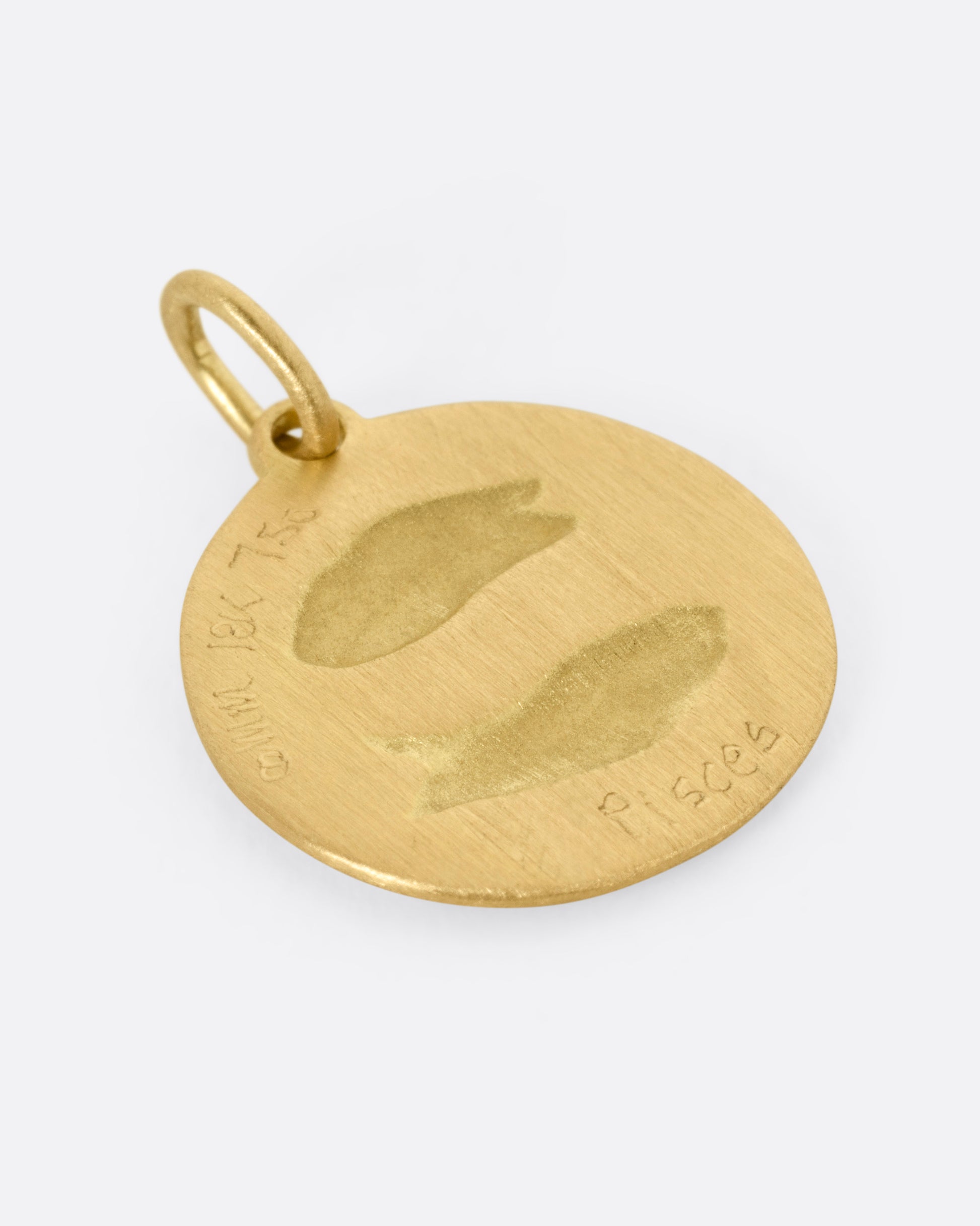 A circular yellow gold Pisces pendant with two fish on its front, shown from the back.
