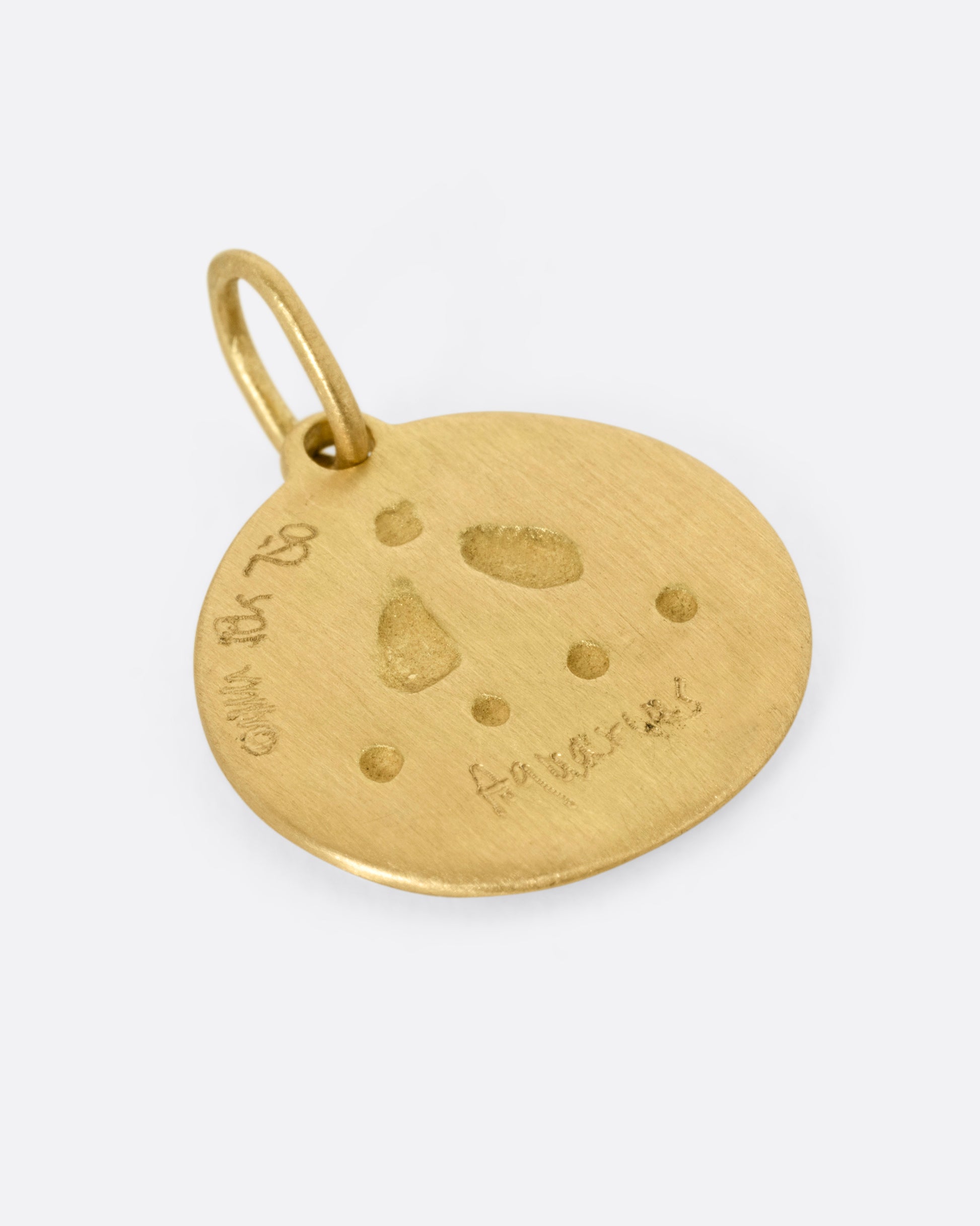 A circular yellow gold Aquarius pendant with the water bearer, shown from the back.