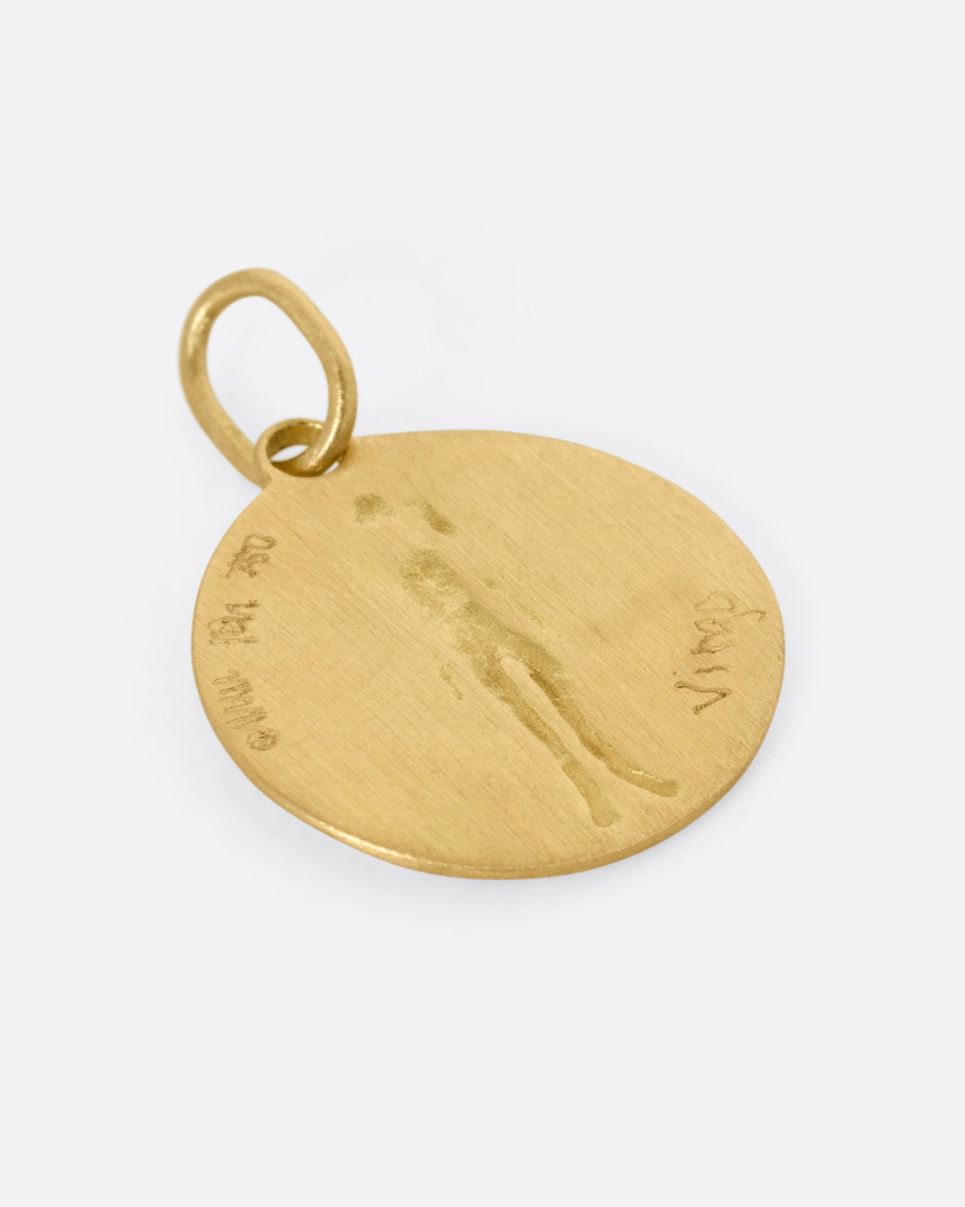 A circular yellow gold Virgo pendant with a female figure, shown from the back.